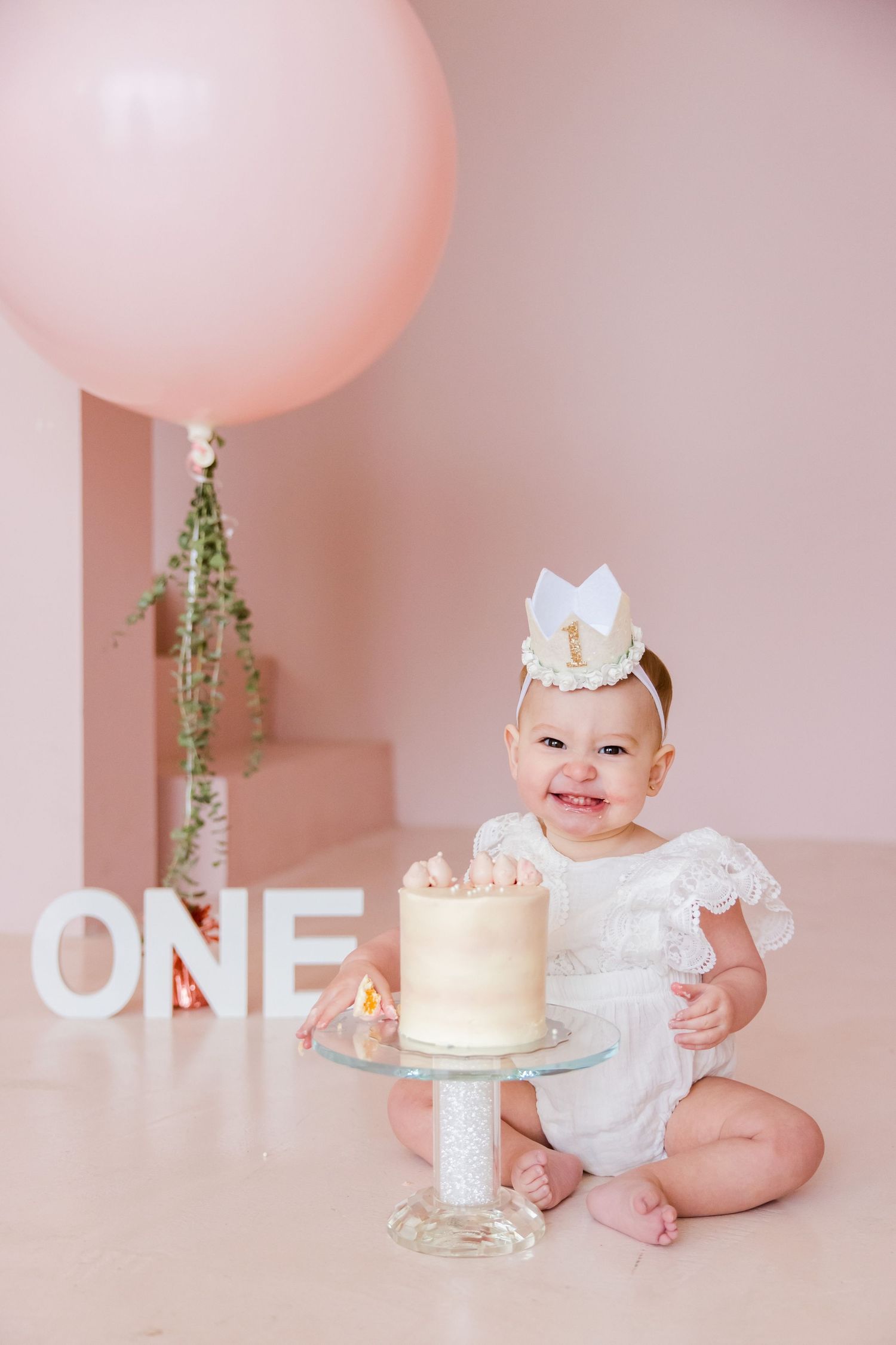 First birthday setup with white cake, pink balloon and sparkling ONE letters.