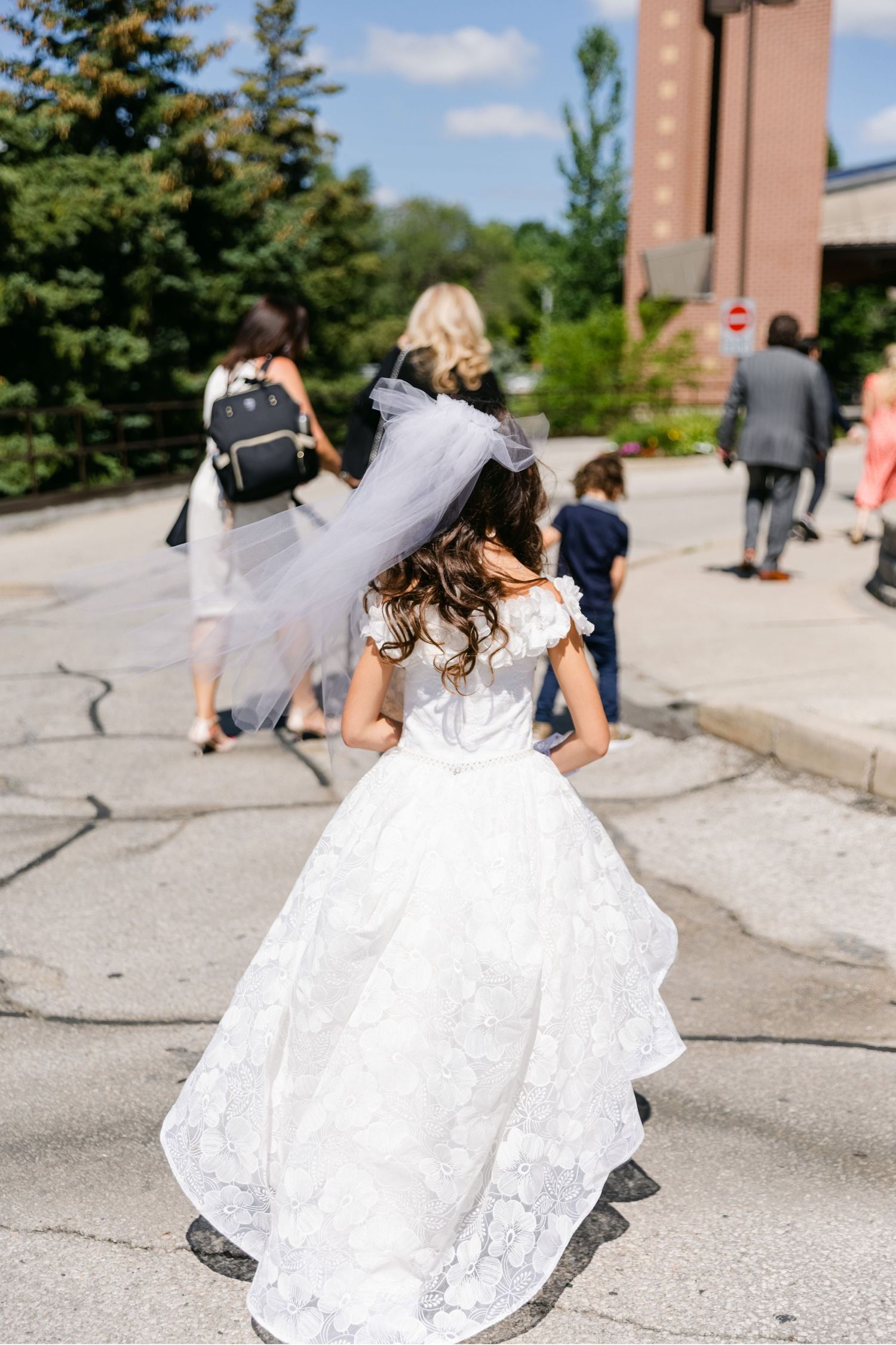 Back view of white lace dress with flowing train walking on outdoor path.