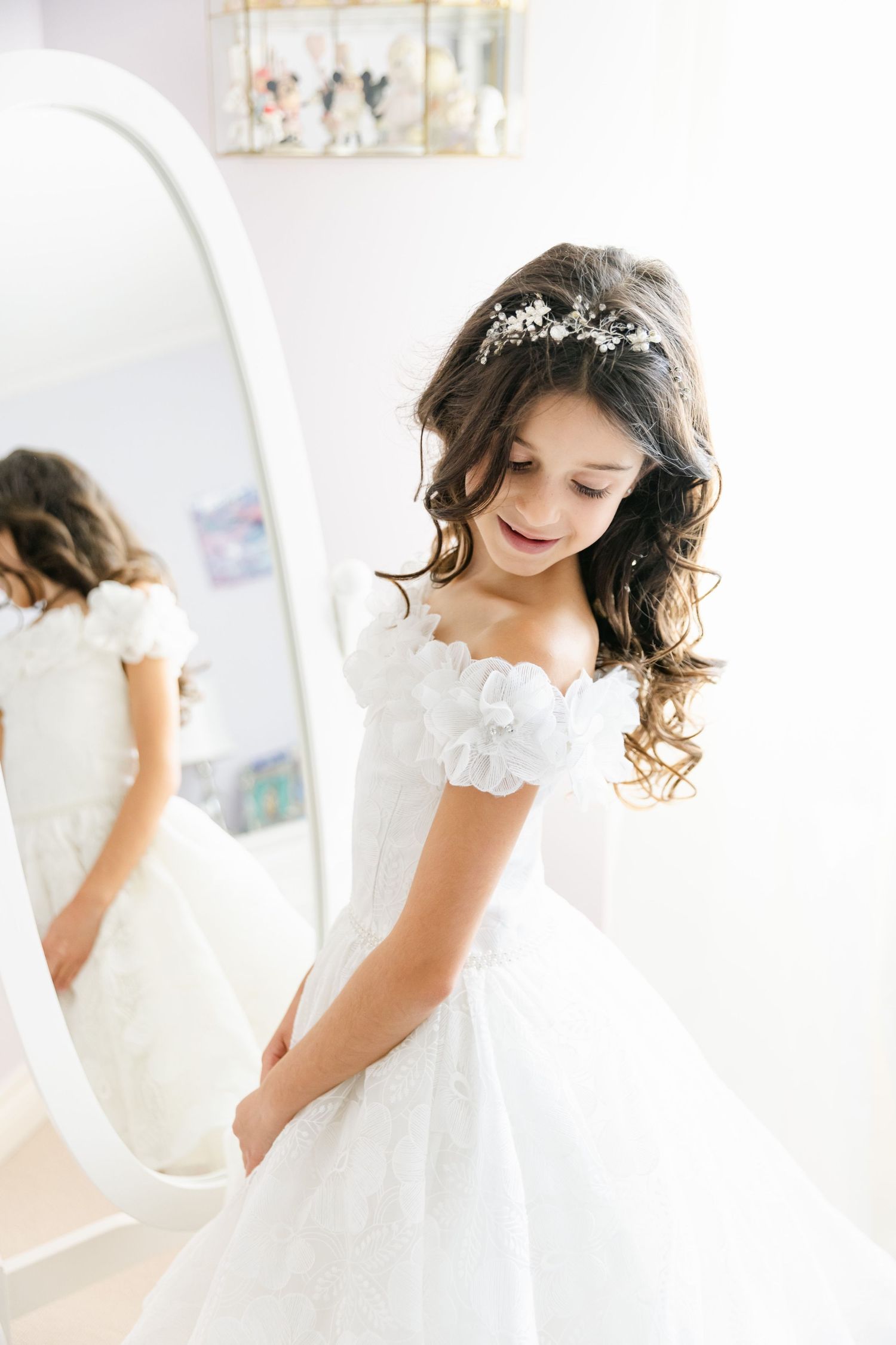 A beautiful white dress sparkles in natural light next to an ornate mirror.