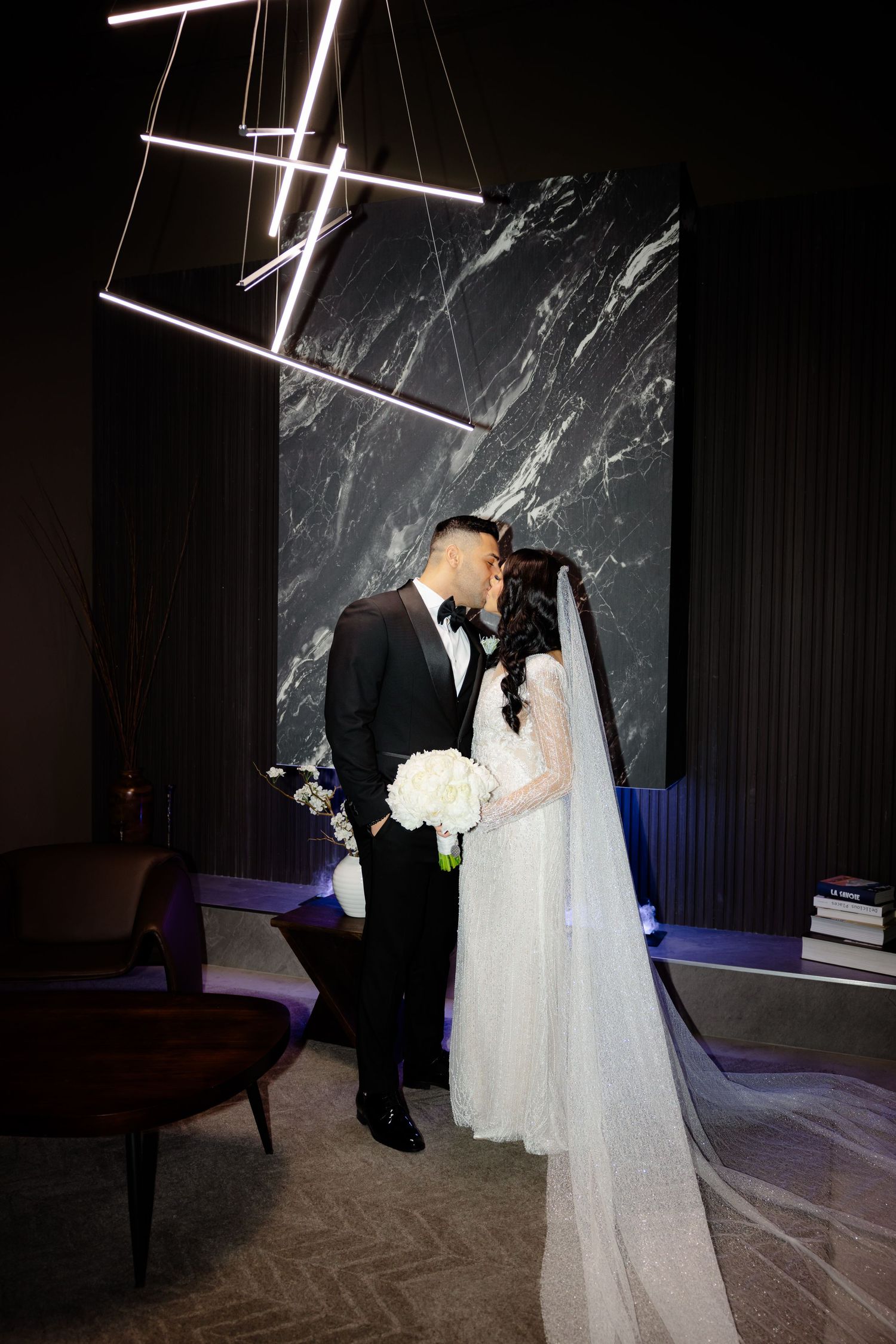 Romantic wedding moment captured under geometric lighting with long flowing veil.