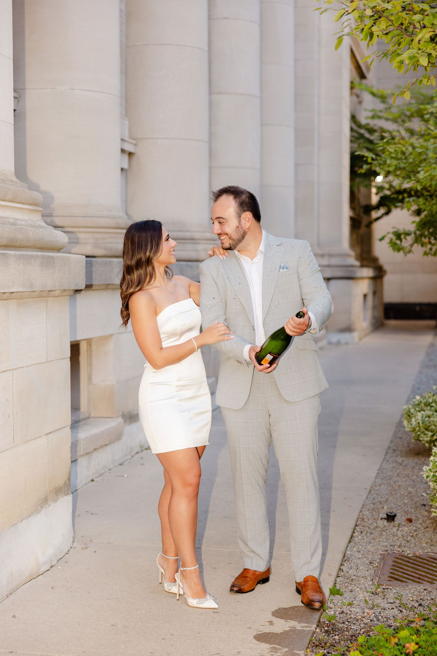 A happy couple in elegant attire shares a romantic moment along a colonnade walkway.