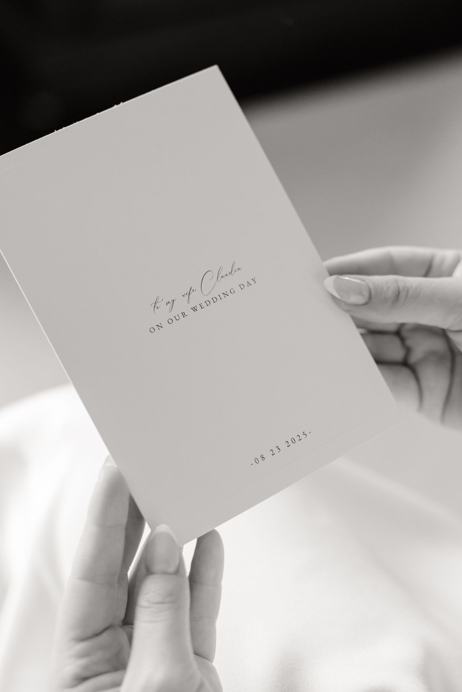 A hand holding a simple white wedding invitation card with elegant handwritten text and minimal design.