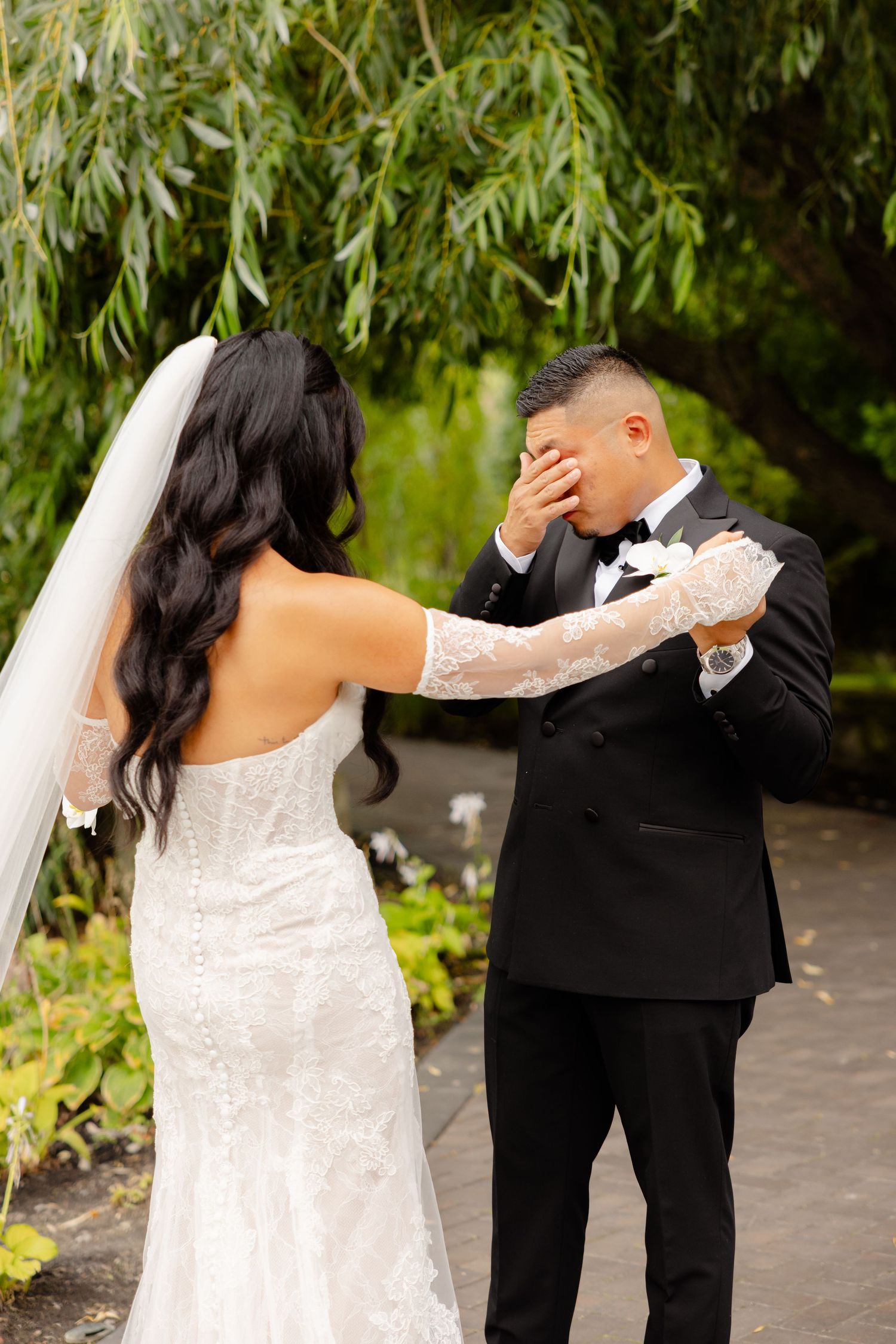 A first look moment at a wedding showing the couple having an emotional reaction in front of willow branches outdoors.