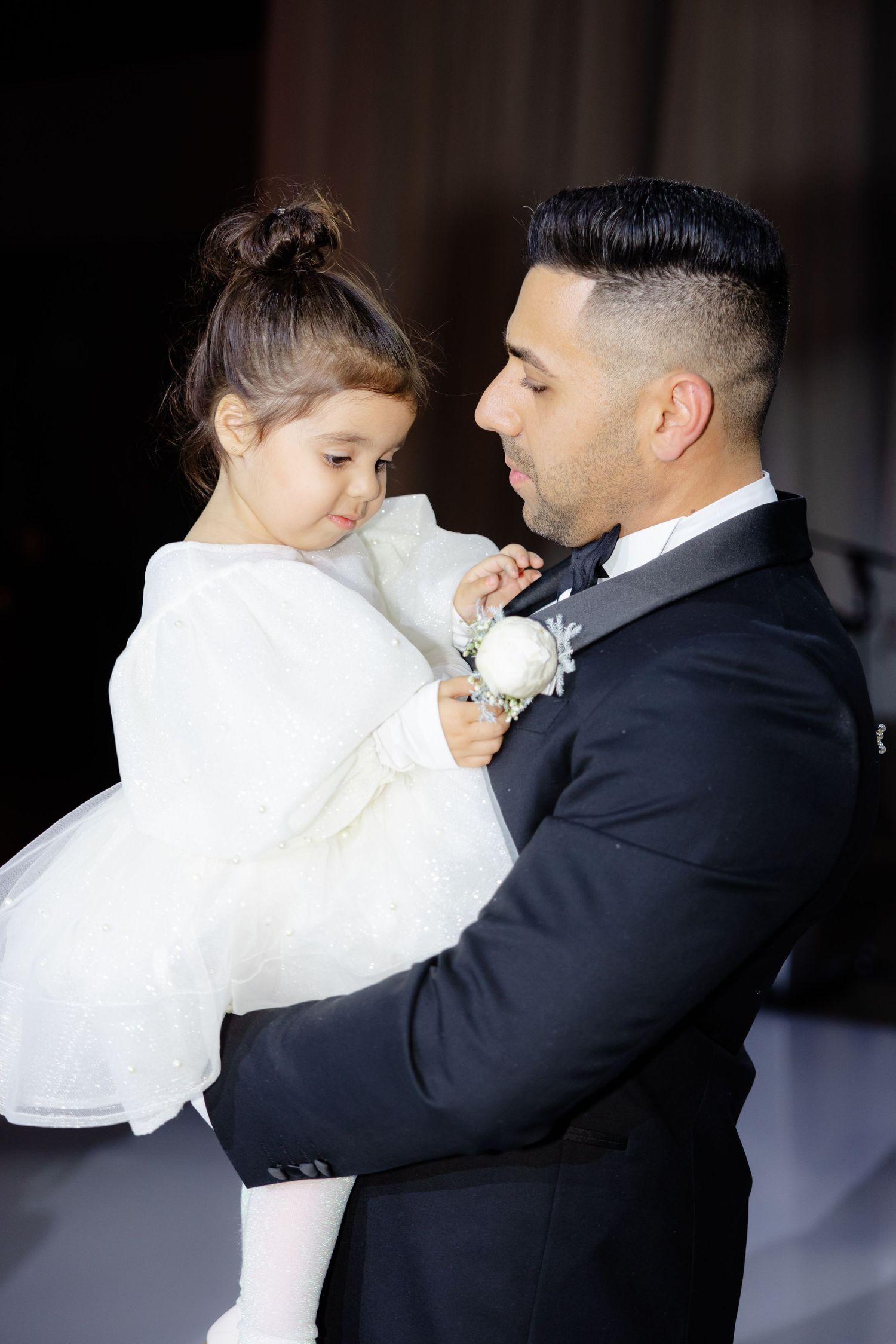 Formal dressed person holds young child wearing white dress at elegant event.
