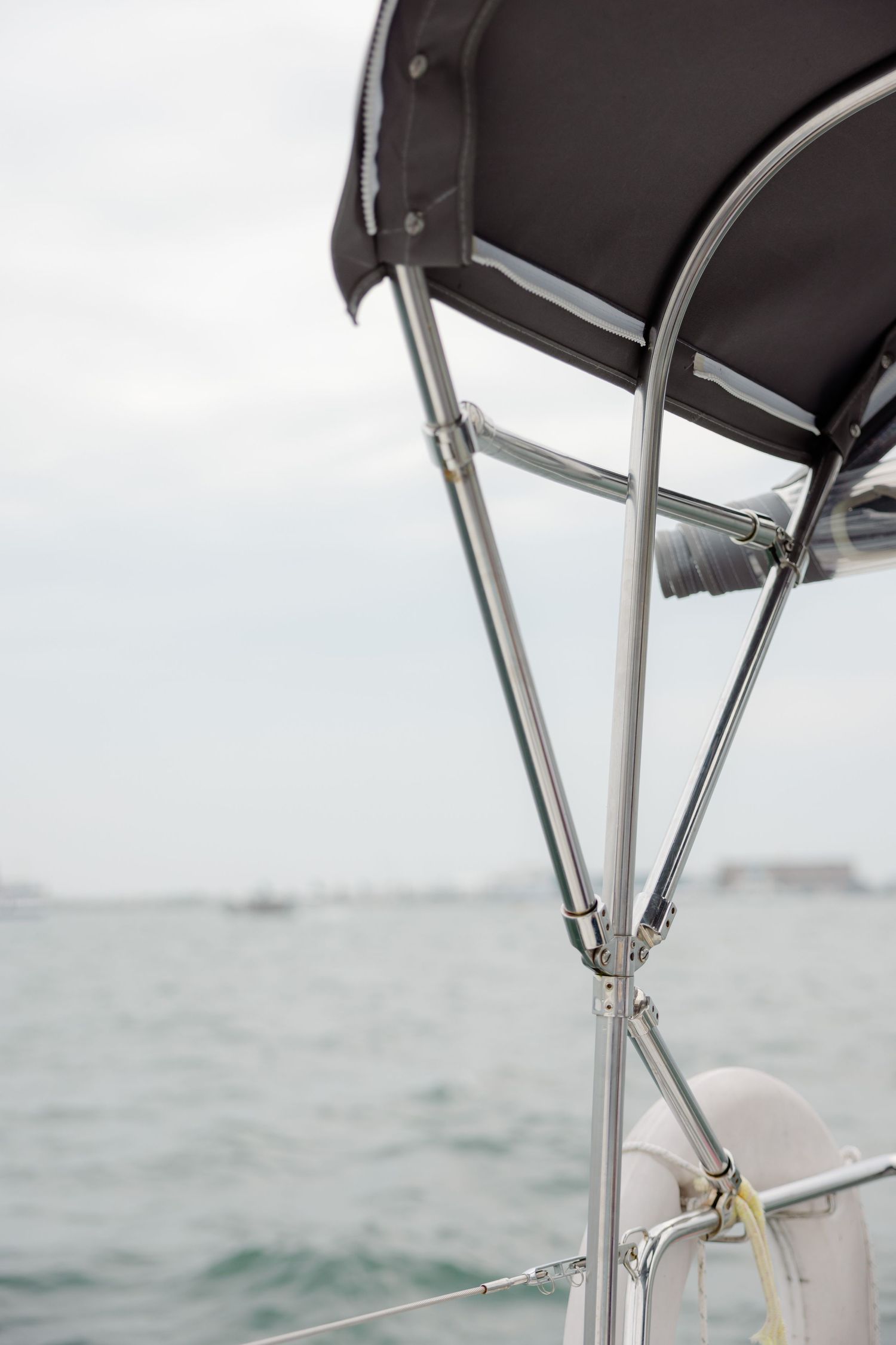 Close-up view of a black boat canopy with metal support frame against an overcast sky and water view.