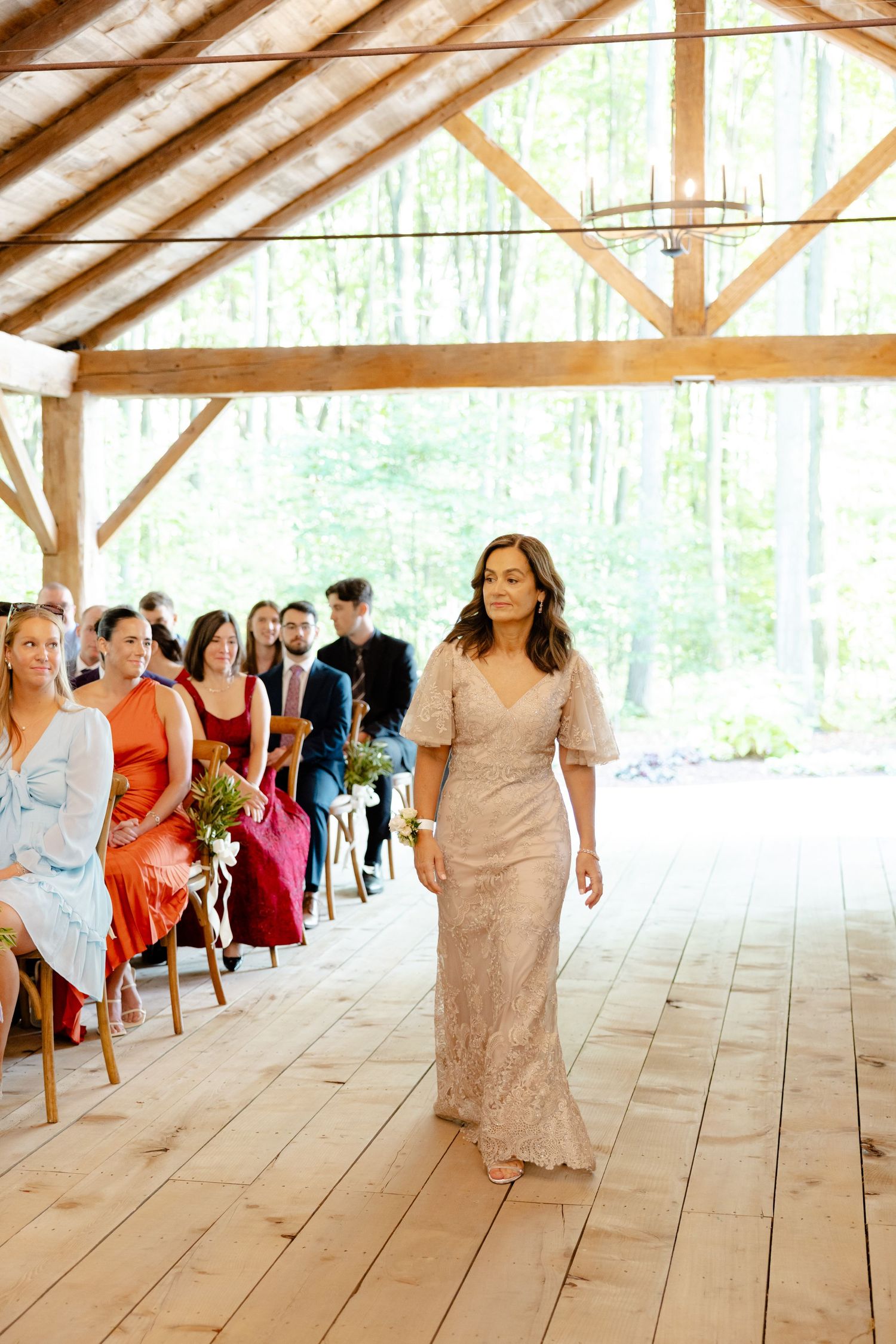 Attendee walking down aisle in beige dress at rustic wooden venue wedding.