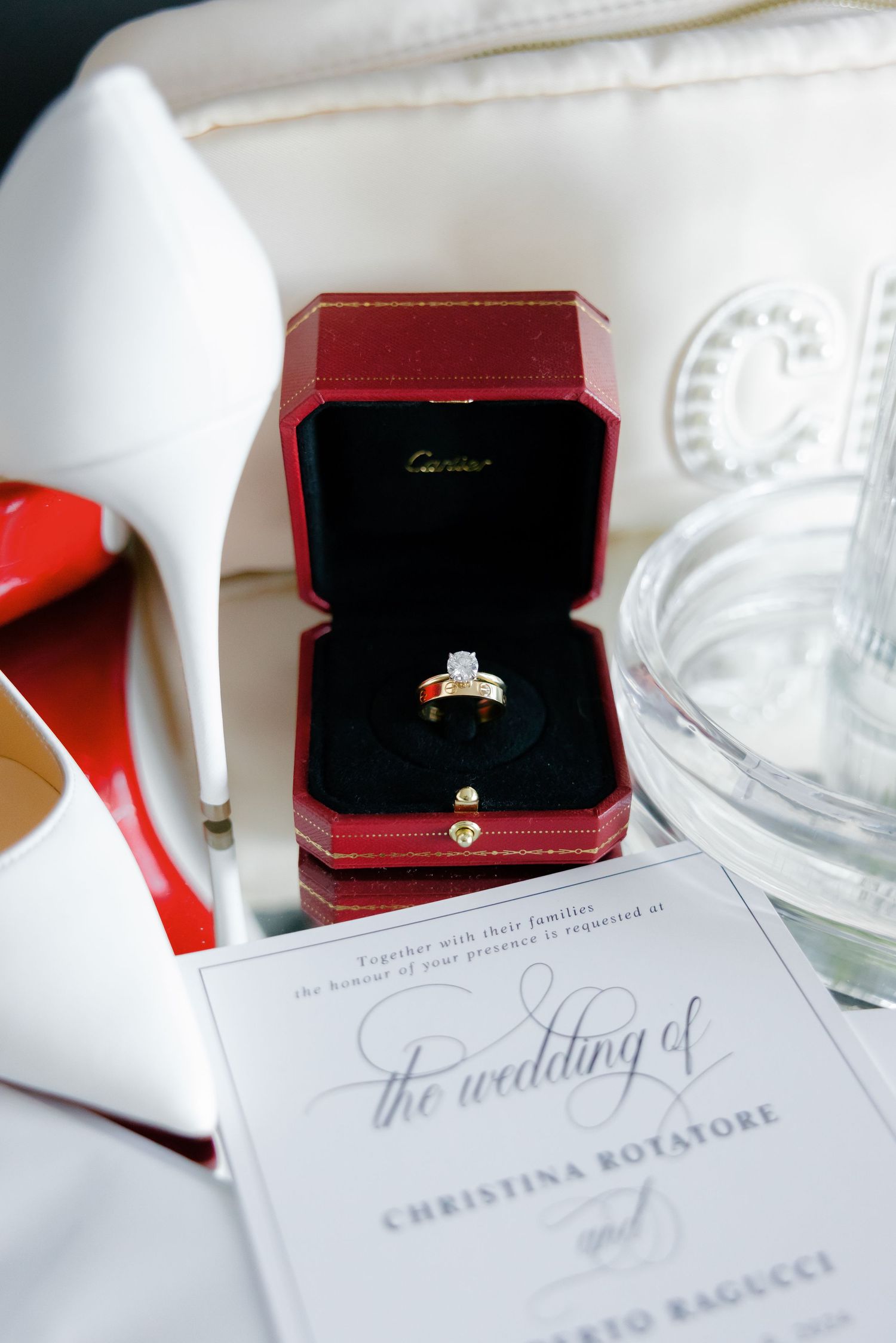 Wedding ring in red Cartier box placed between white heels and wedding stationery.