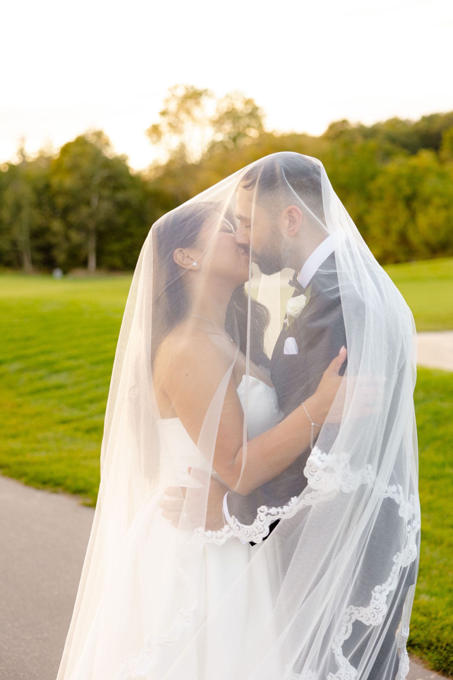 Golden hour wedding photo with couple sharing tender moment under sheer veil.