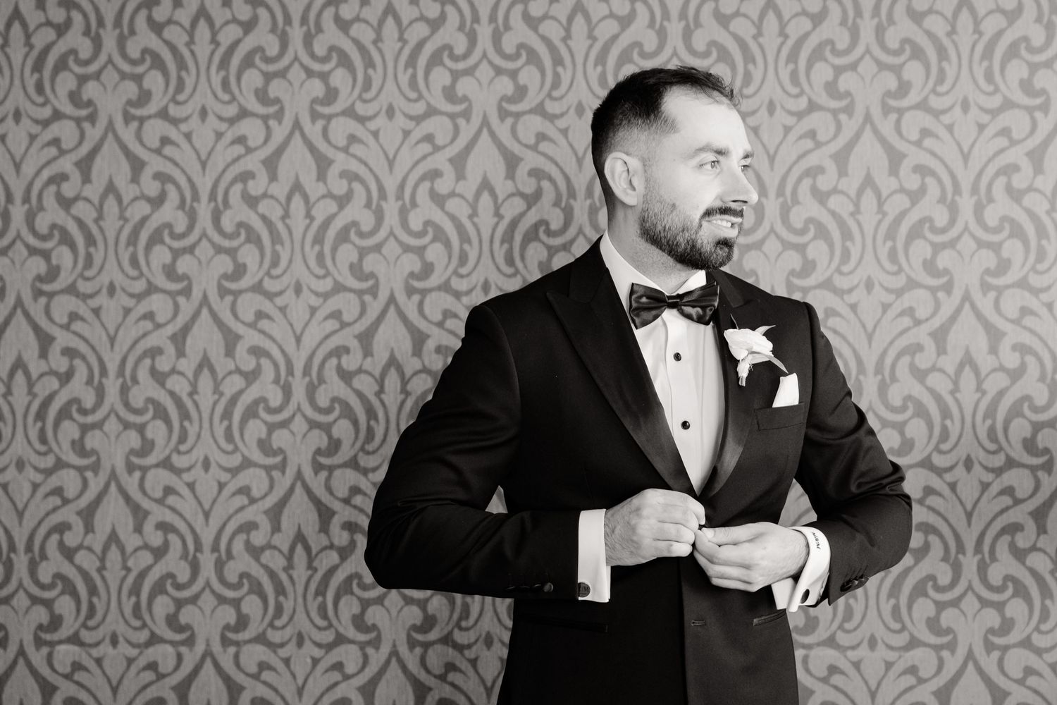 Sharp black and white portrait of groom in classic tuxedo against patterned wall.