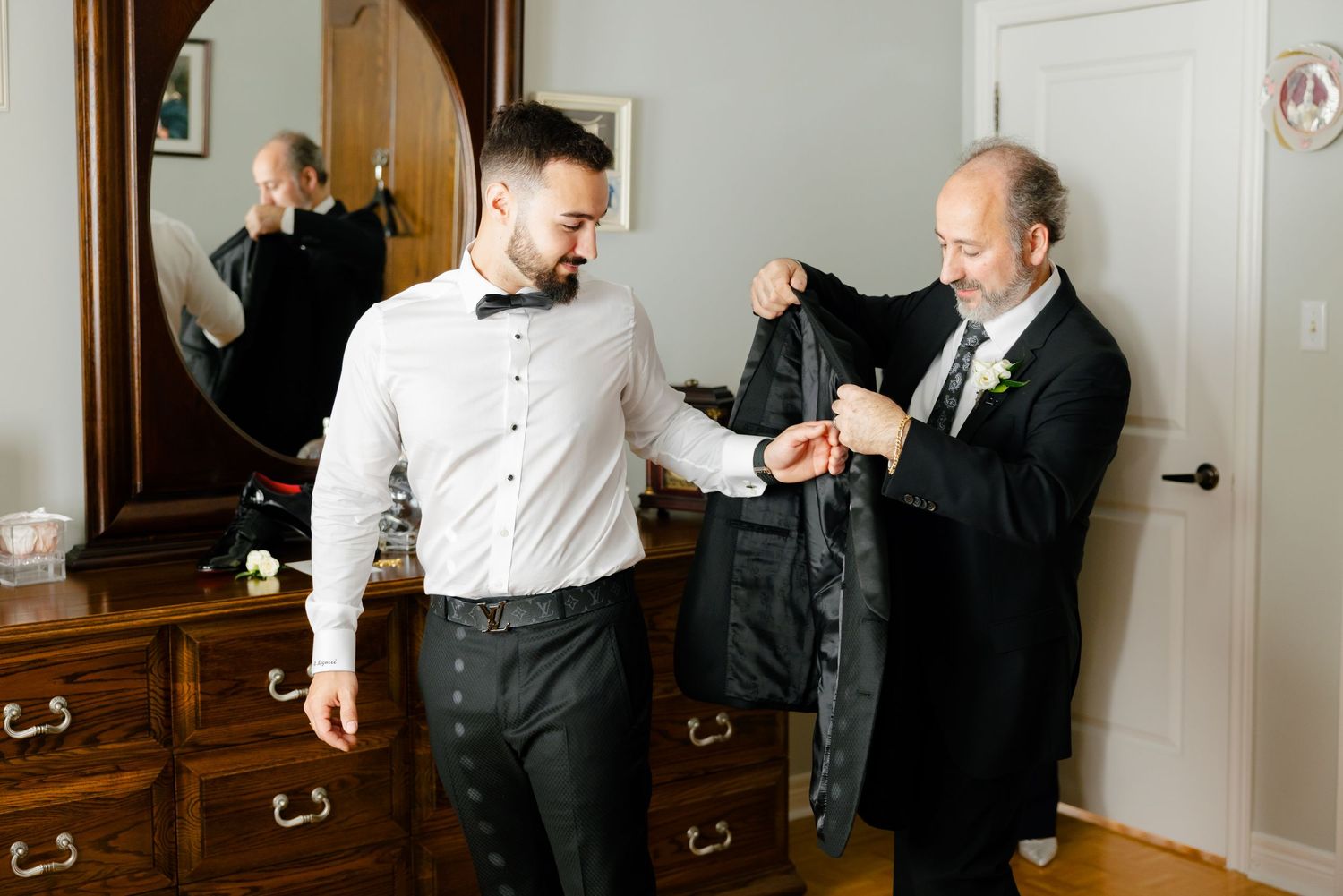 Wedding preparation scene showing formal attire being adjusted near wooden furniture.