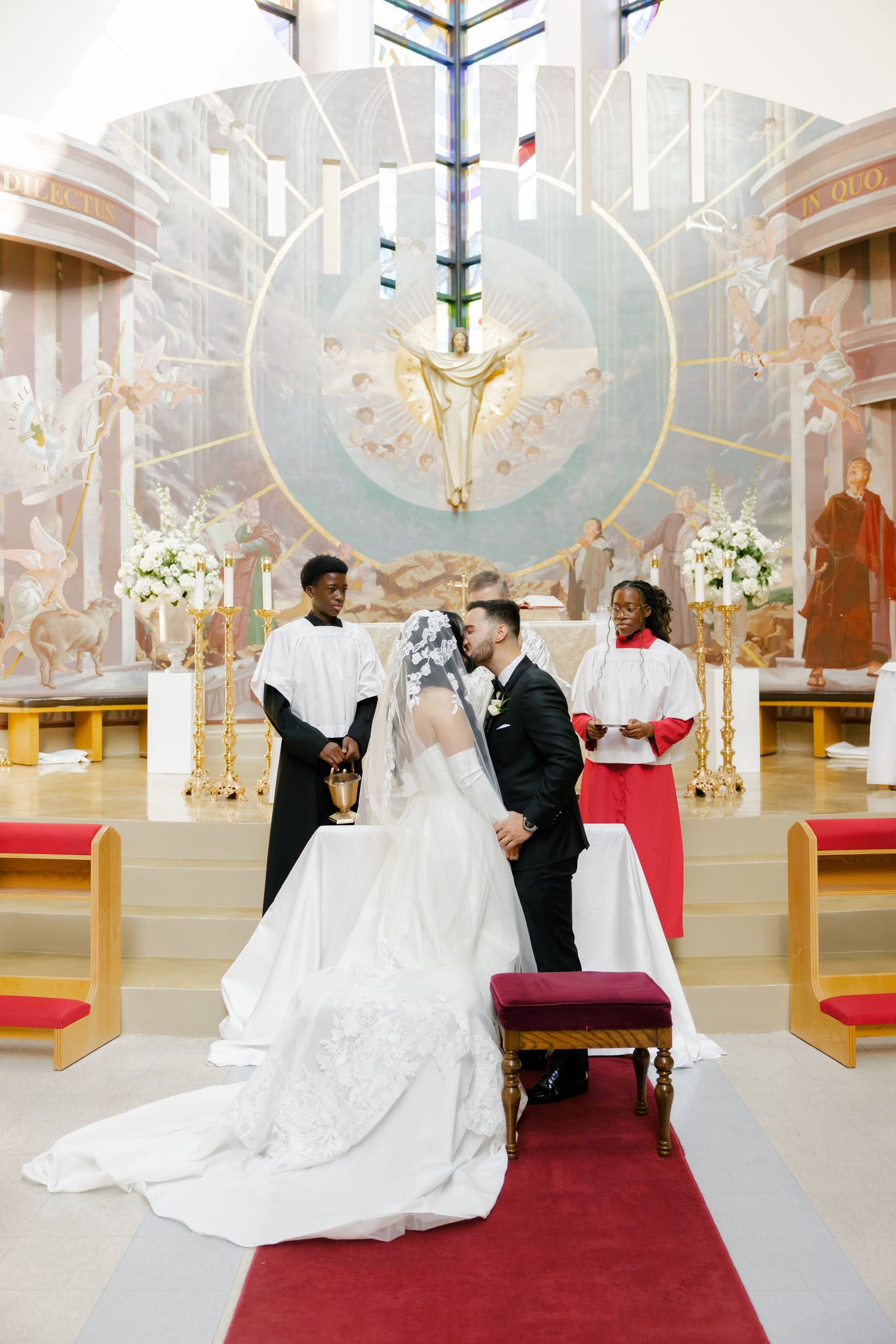 A wedding ceremony in progress inside a church with elegant decorations and a red carpet aisle.
