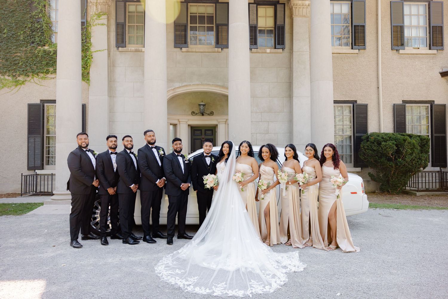 Bridal party in black suits and champagne dresses posed before a classic architectural backdrop.