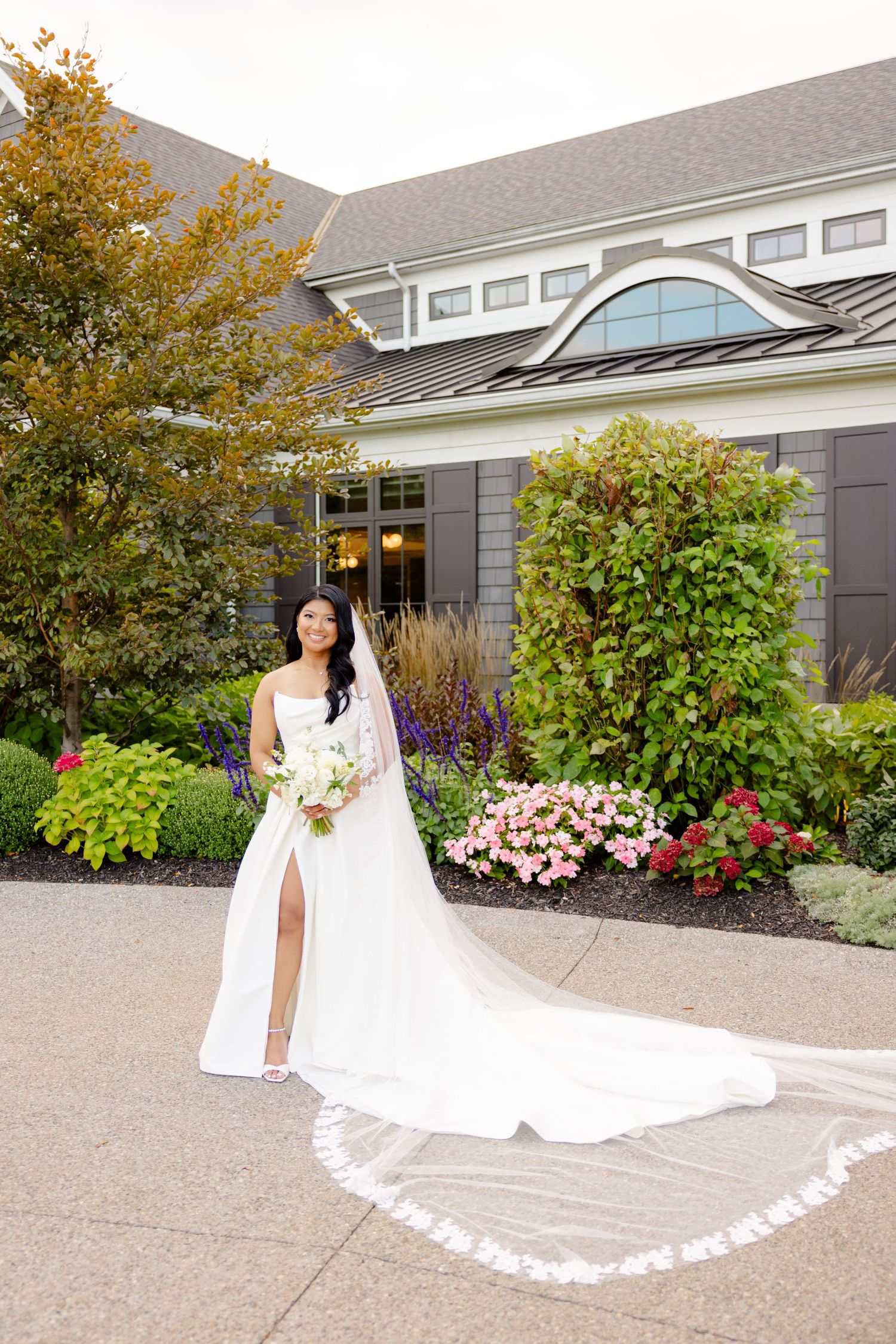 Bridal portrait showing full-length view of white wedding dress with dramatic train in garden setting.