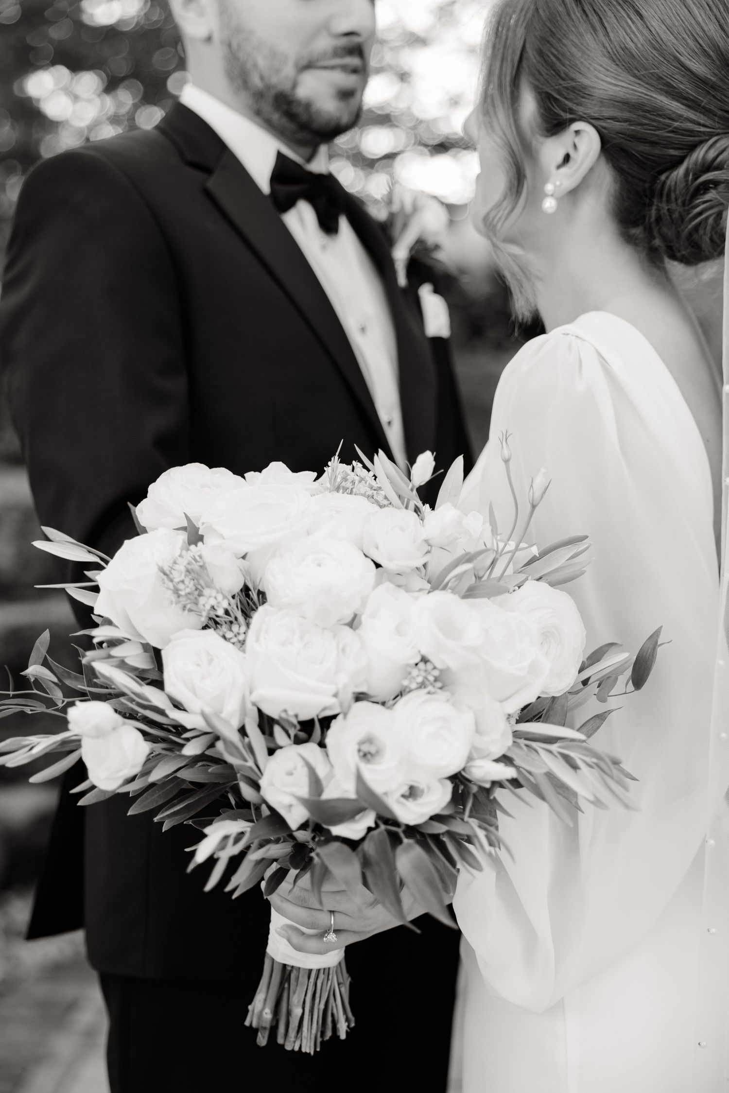 Black and white photo showing elegant white peony bouquet between bride and groom.