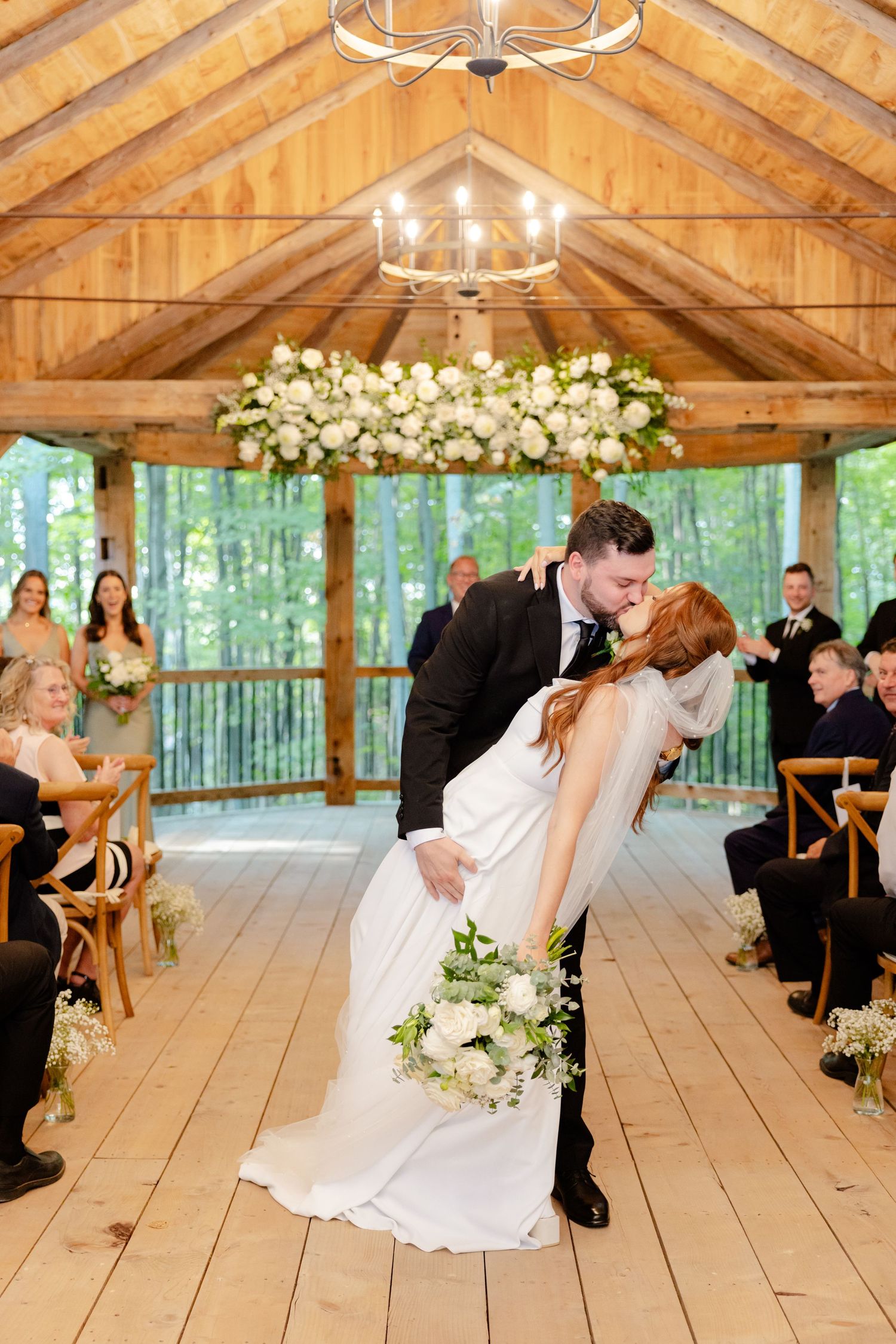 A romantic dip kiss during a wedding ceremony in a rustic wooden pavilion with forest views.
