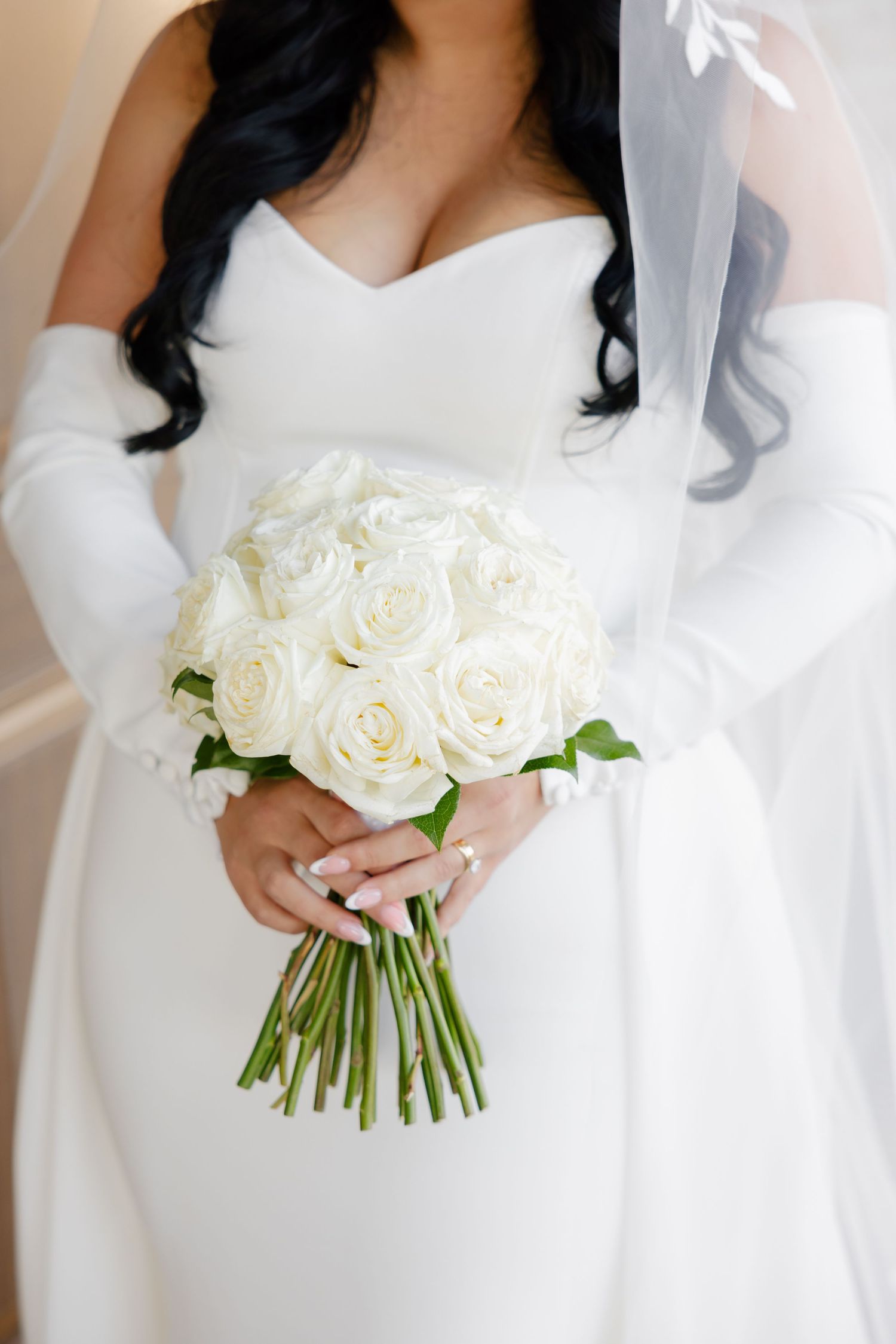 Close-up of white rose wedding bouquet held by bride in white dress.