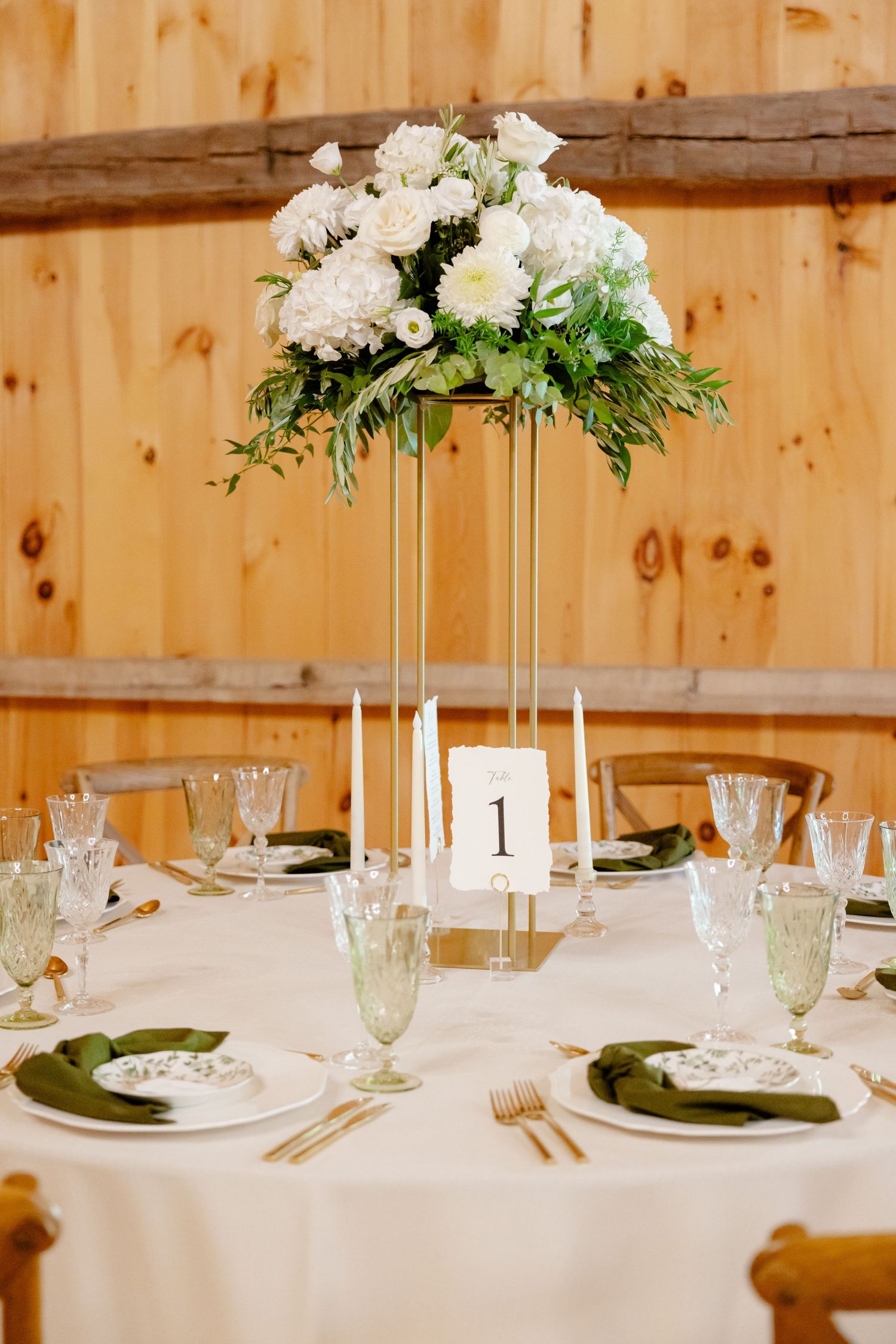 Elevated white floral centerpiece with tall gold stand on round wedding reception table.