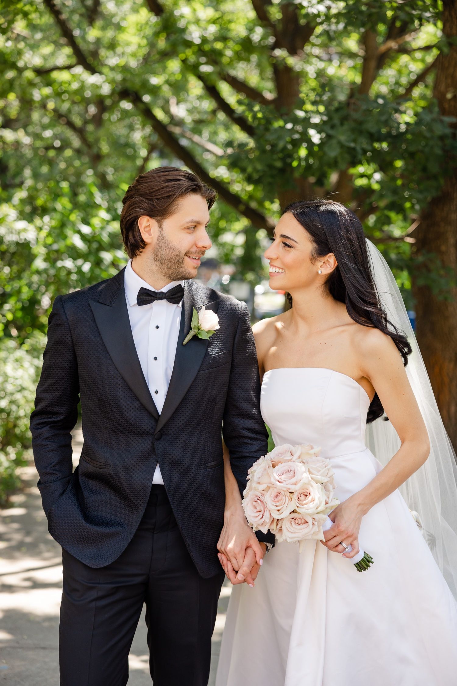 Wedding couple shares intimate moment under green canopy of trees.
