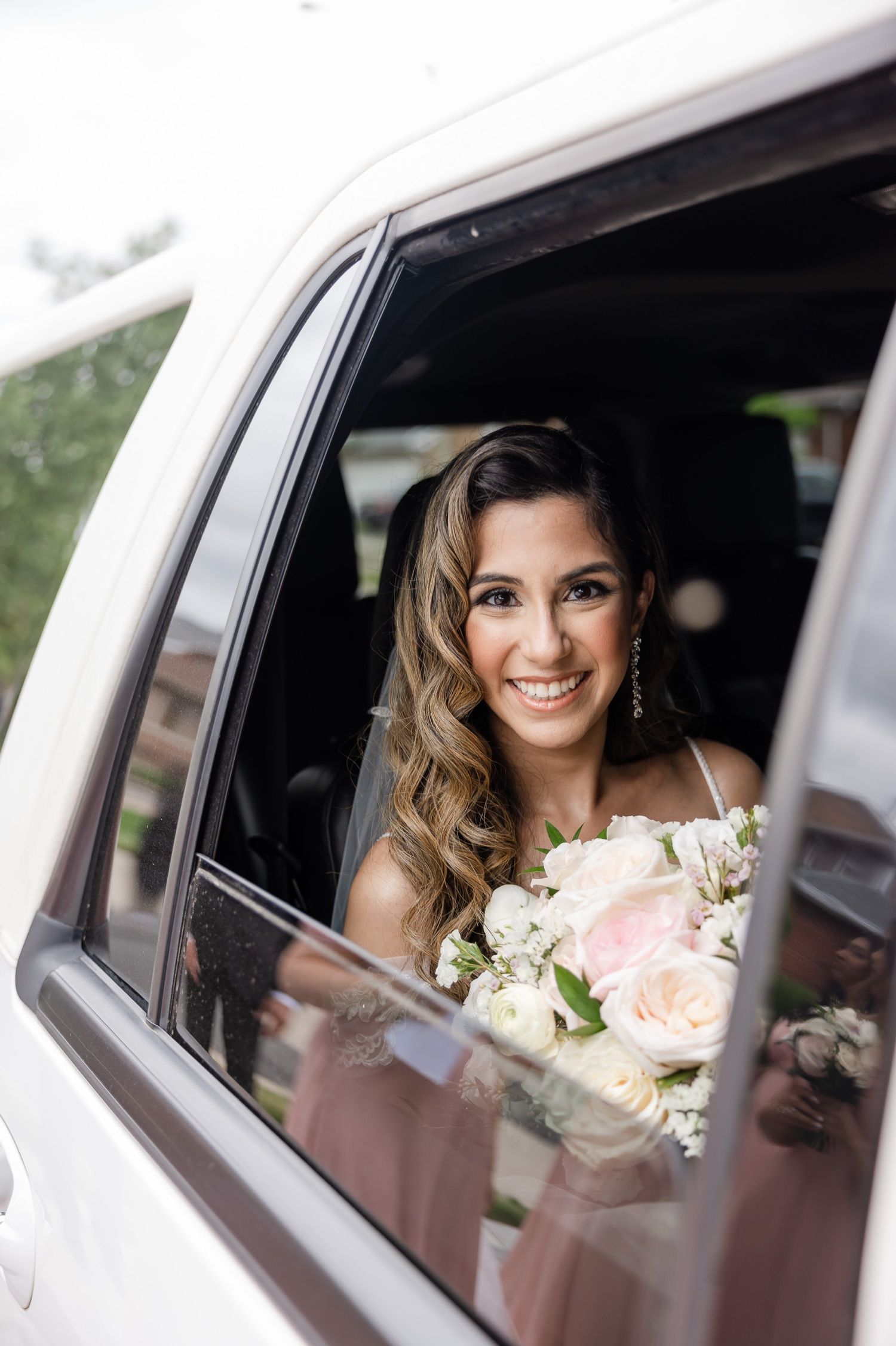 Happy bride with flowing hair and bouquet sits in white wedding limousine.