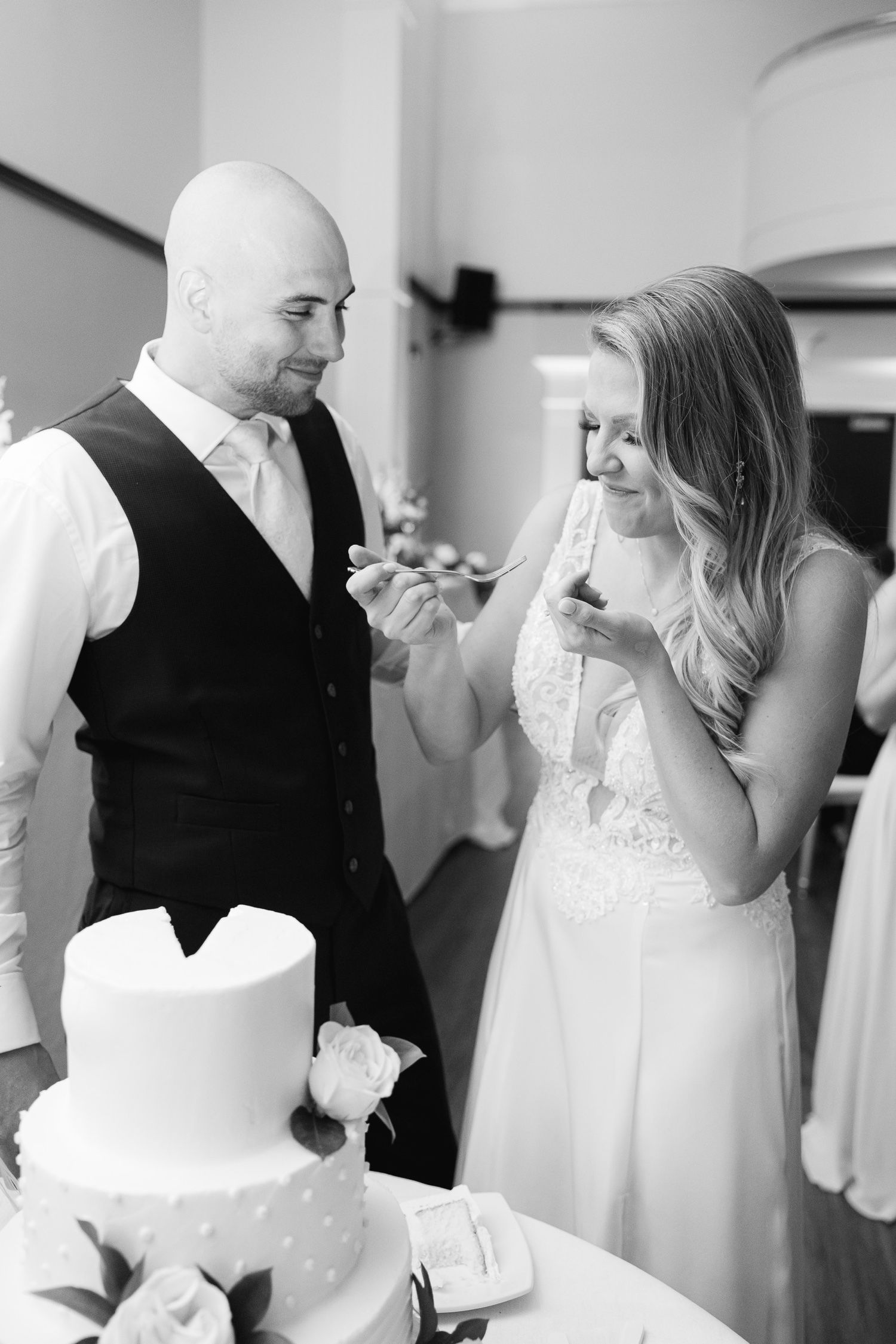 A black and white photo of a couple sharing wedding cake during their reception celebration.