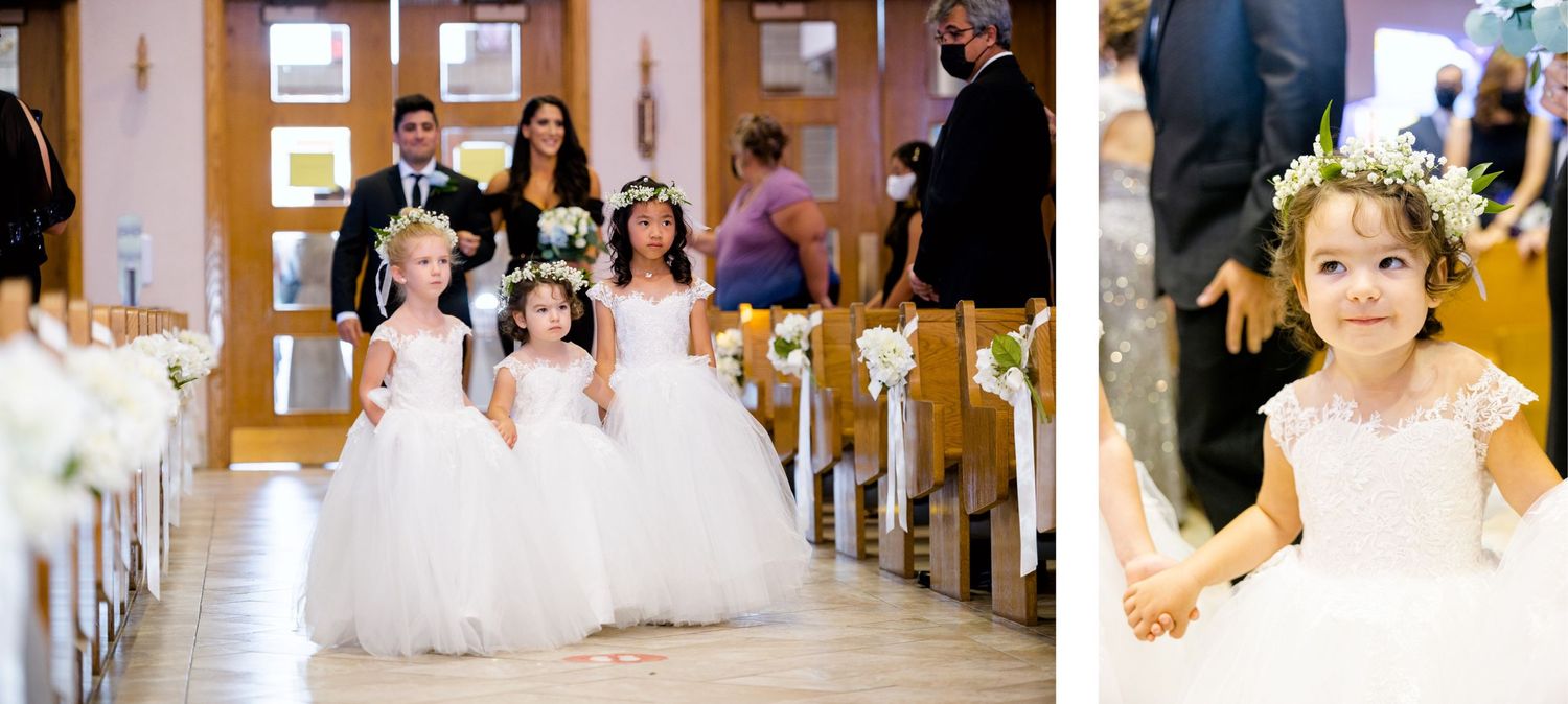 Young flower girls in white dresses walking down a church aisle decorated with floral arrangements.