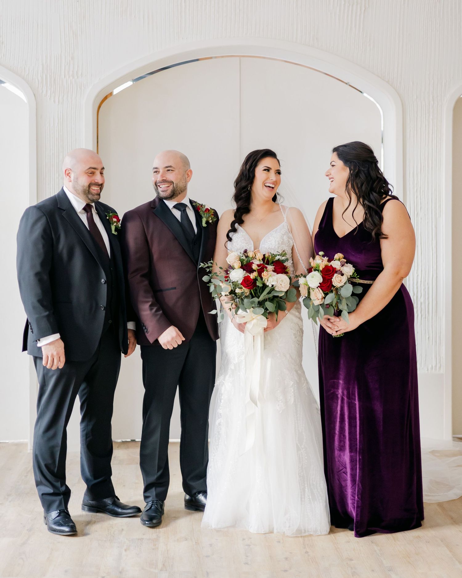 Wedding party poses together under white archway in formal attire.