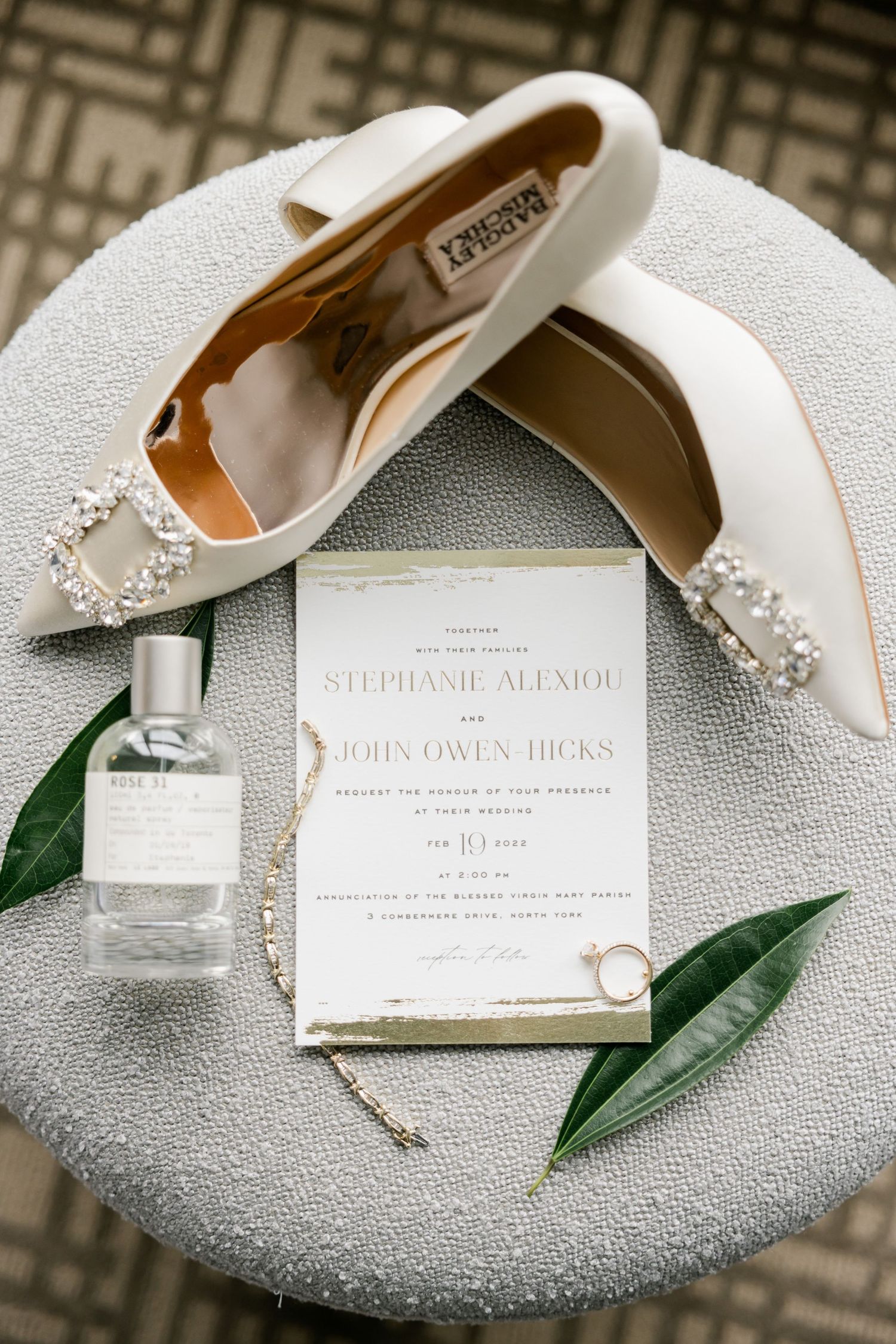 White wedding shoes and invitation styled with greenery on grey ottoman.