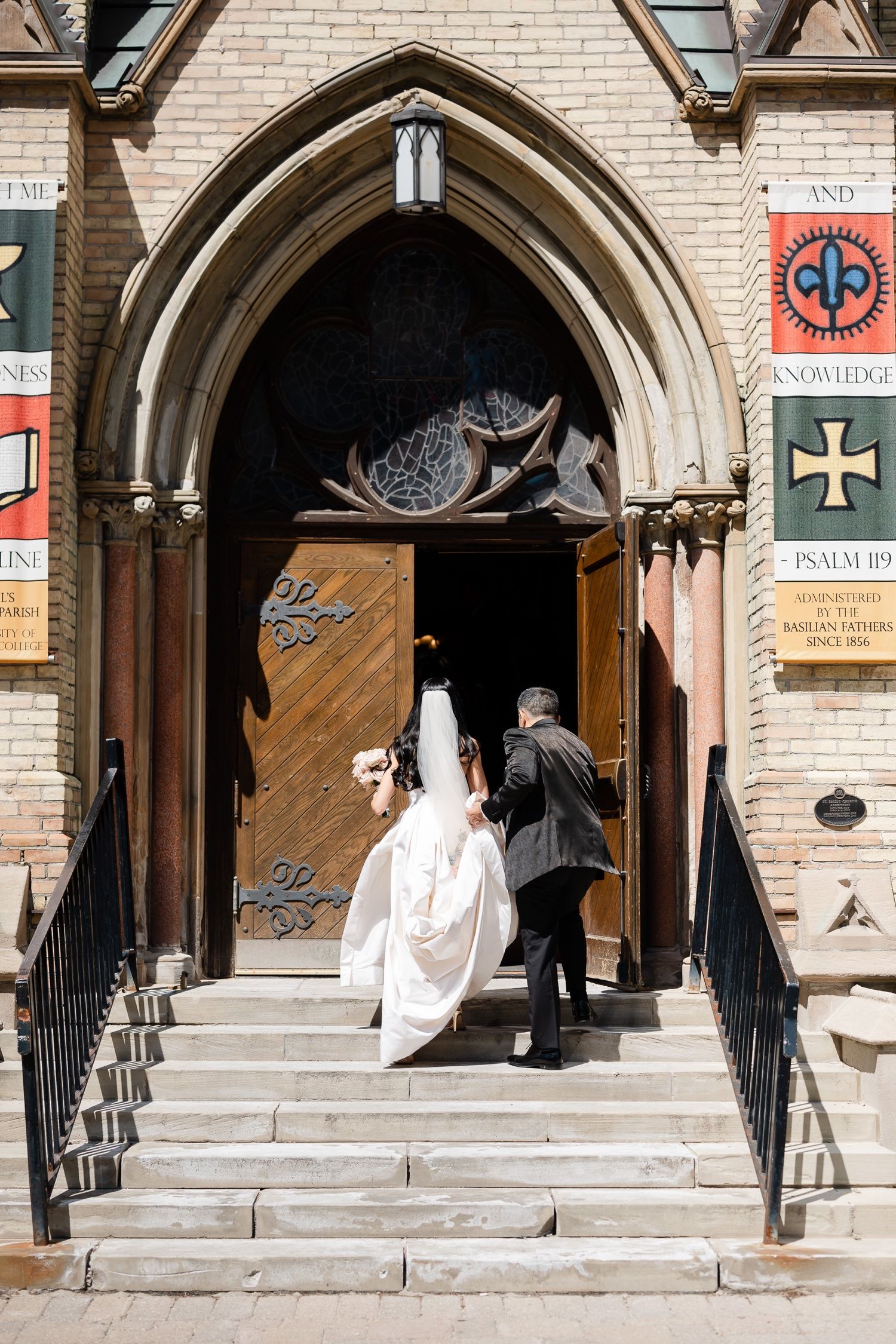 A couple entering through an ornate gothic church doorway with decorative stone archway and steps.