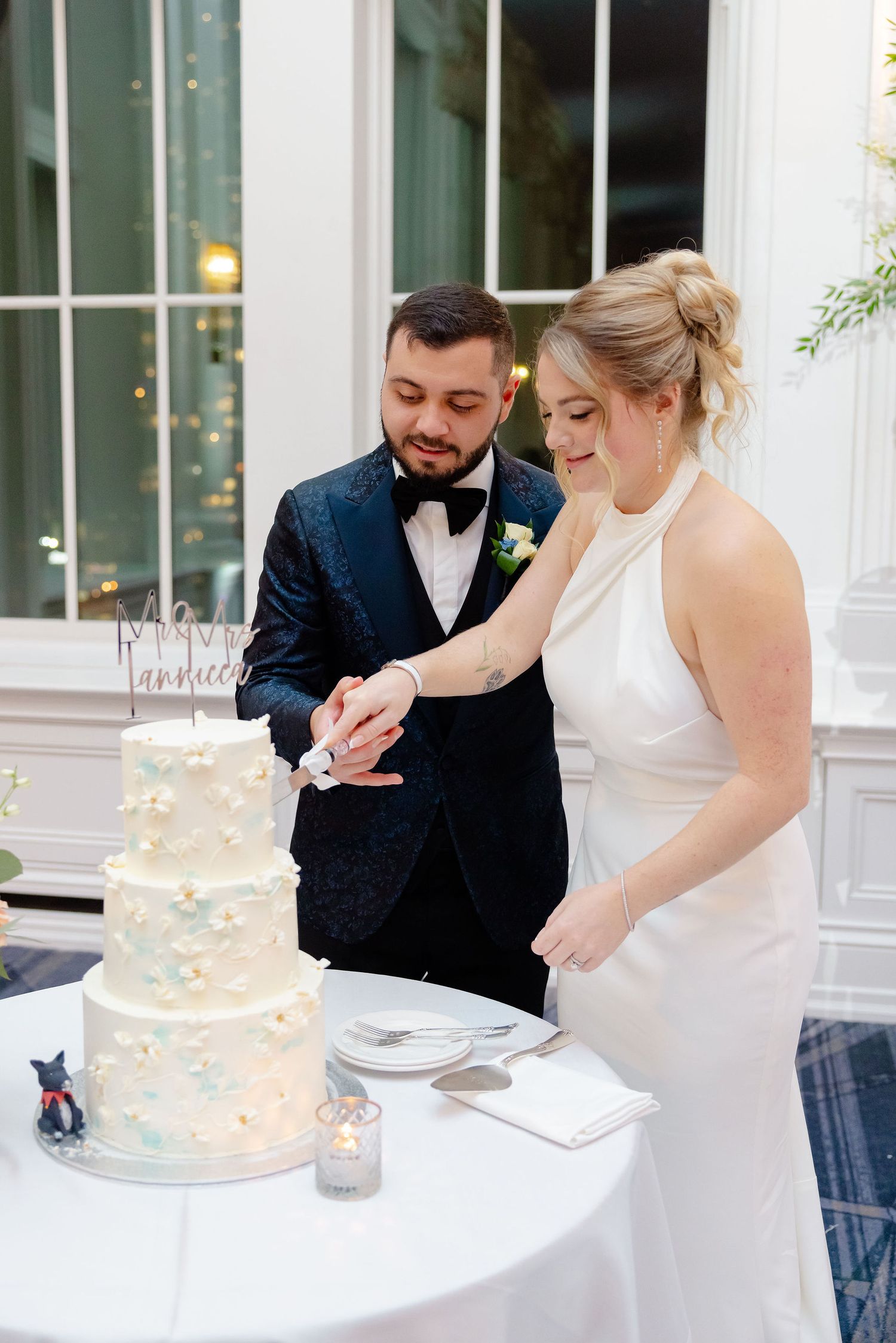 Couple cutting their elegant white wedding cake together at an indoor reception venue.