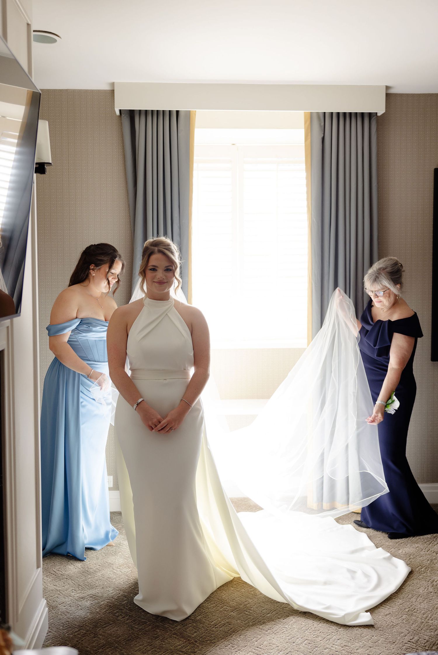 Wedding preparation scene with bridesmaids in blue and navy dresses helping with final touches.
