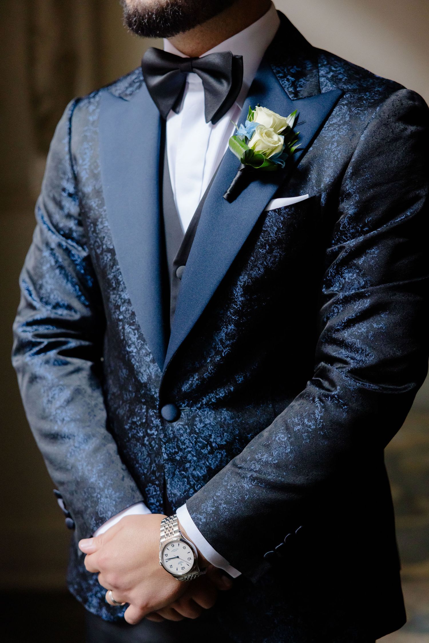 Details of groom's navy blue textured tuxedo jacket with black bow tie and boutonniere.