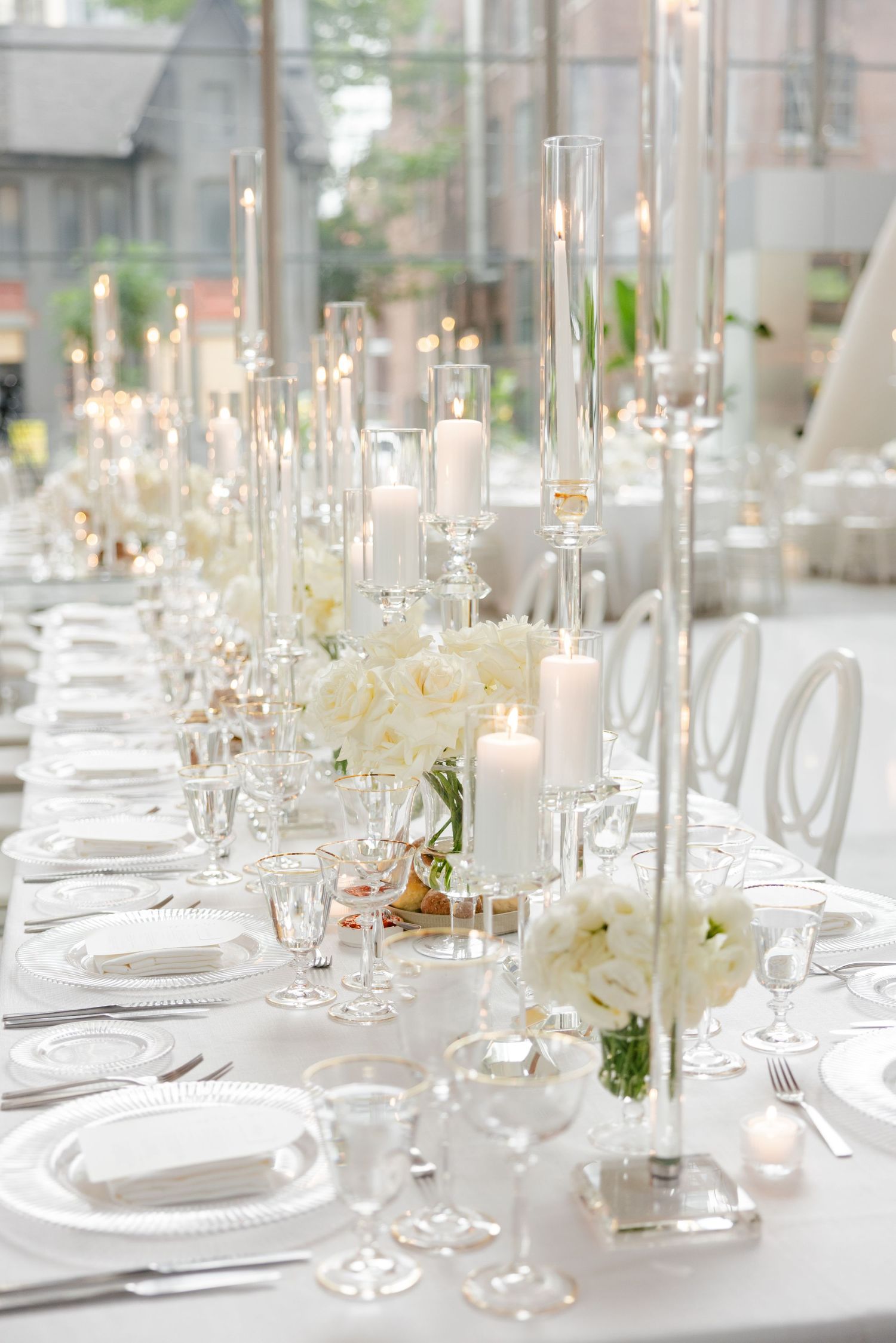 Elegant white table setting with glass candleholders and white floral arrangements for a wedding reception.