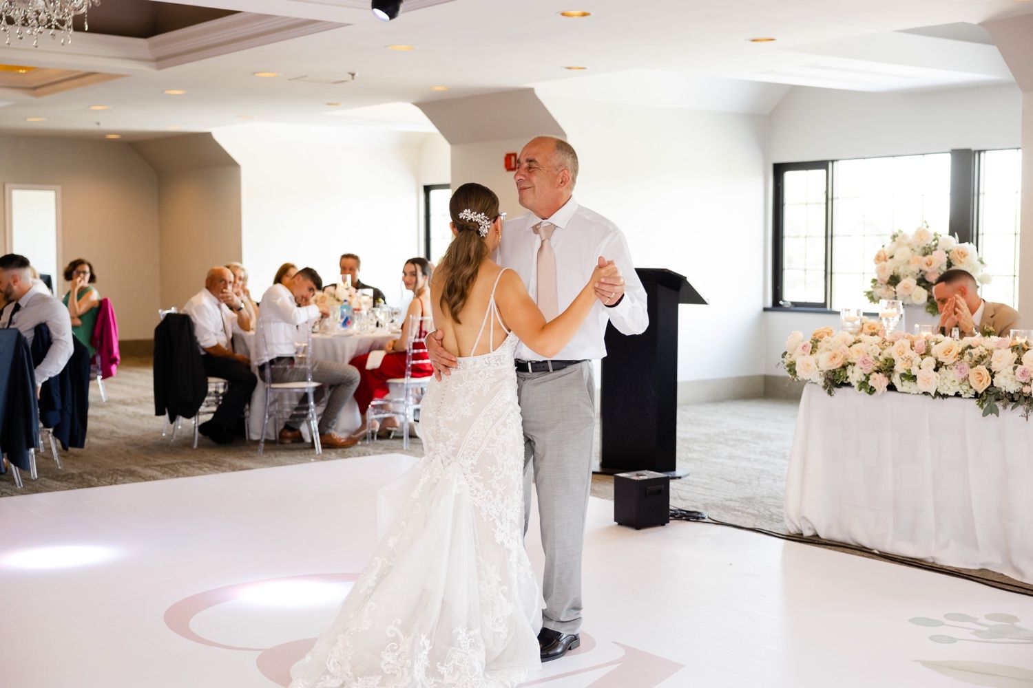 Elegant wedding dance moment on a white dance floor with floral arrangements in the background.