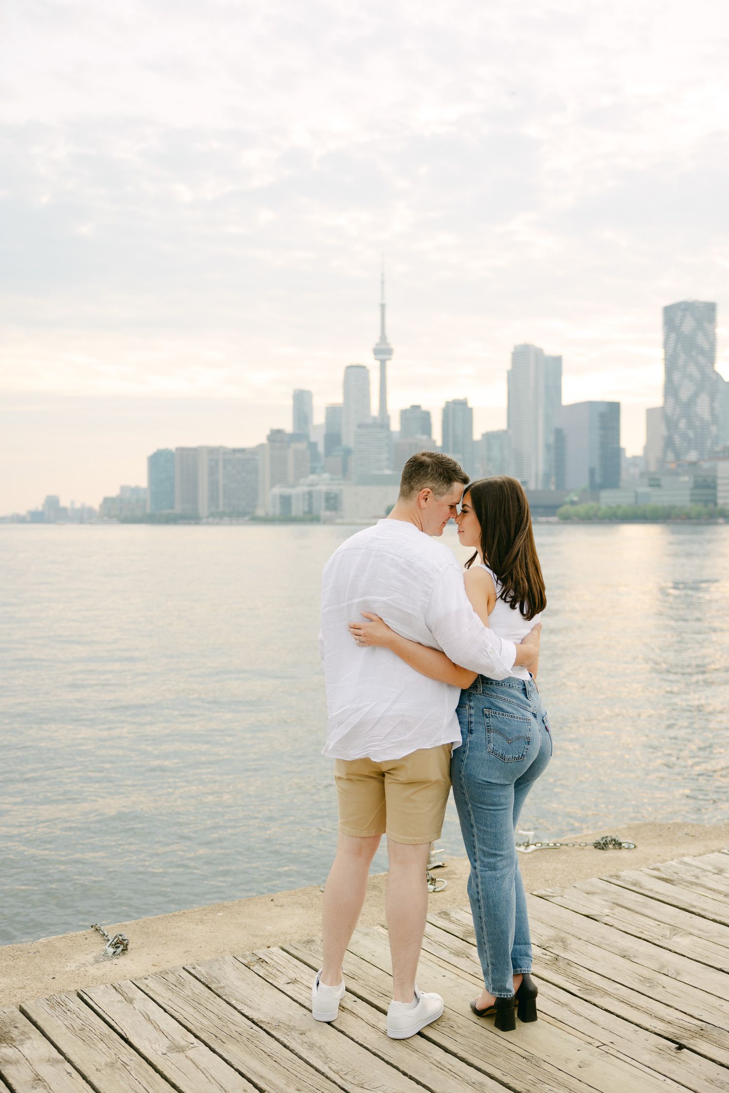 A couple shares an intimate moment on a pier overlooking Toronto's iconic waterfront skyline.