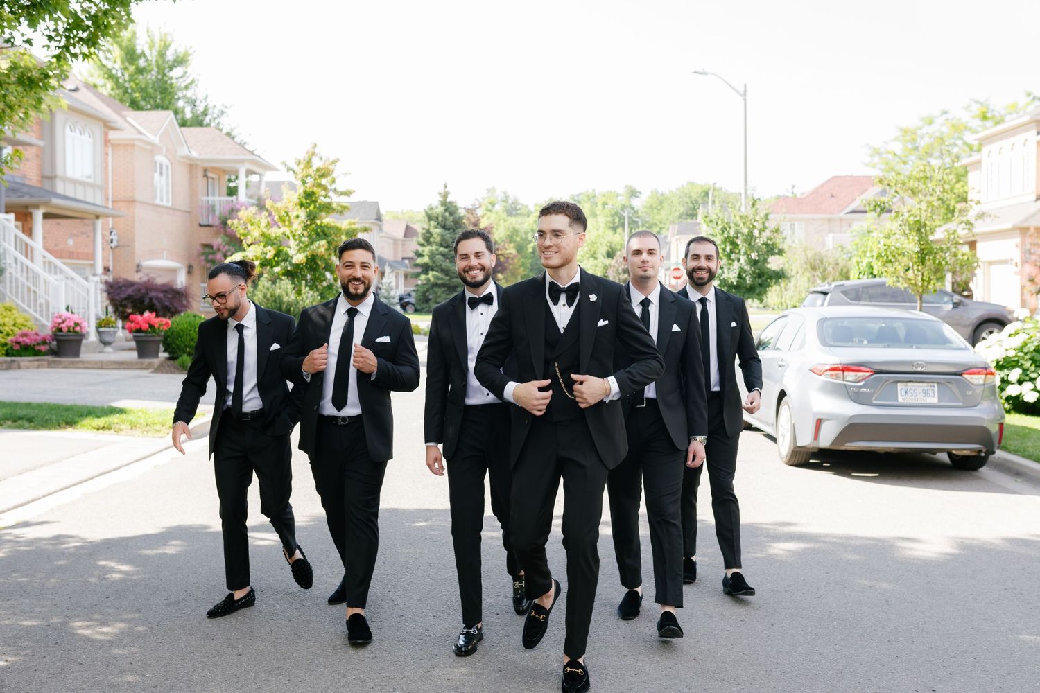 Wedding party in black suits walking together down sunny suburban street.