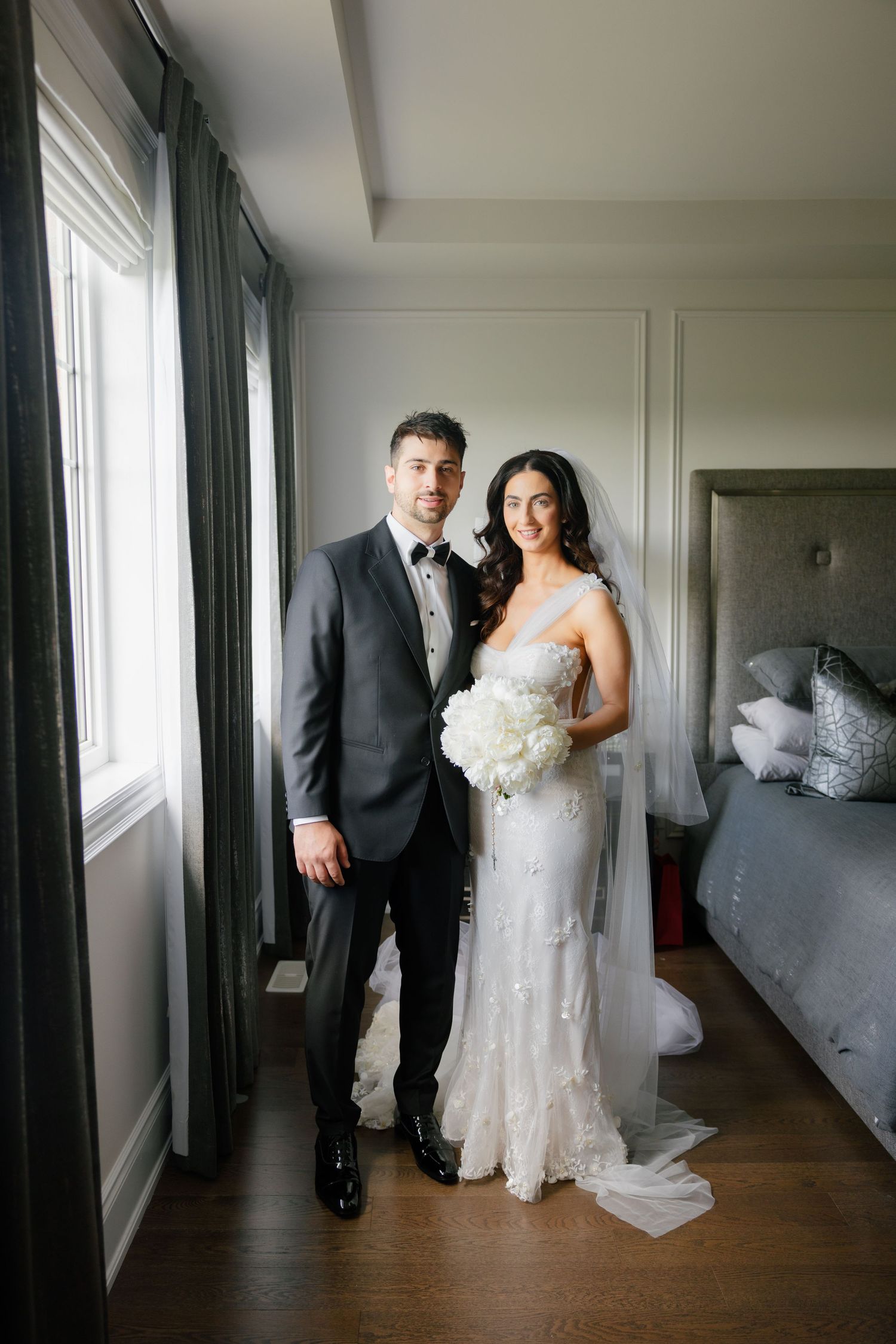 A wedding couple posing by a window in a hotel room with elegant green curtains.