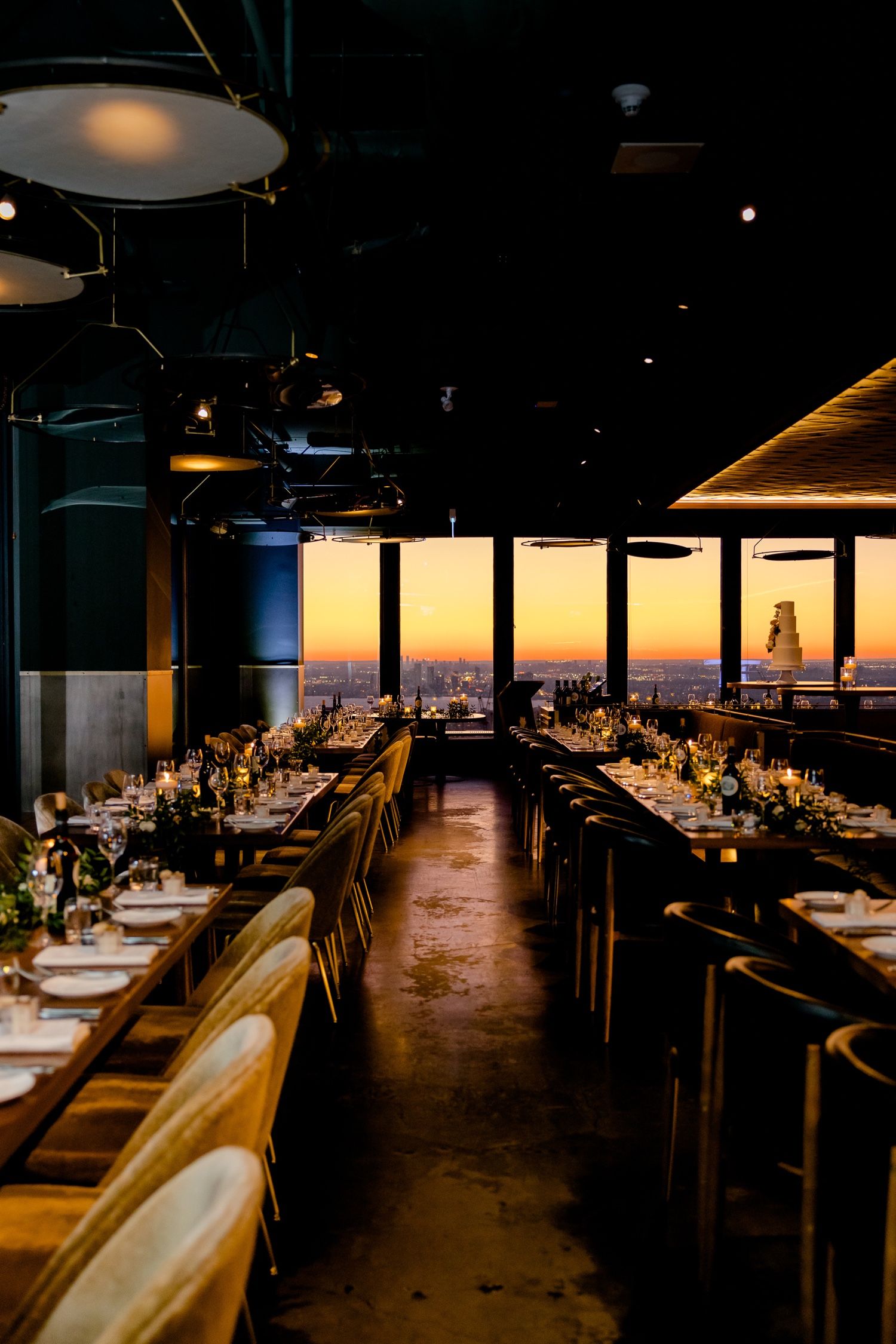Modern restaurant interior setup for wedding reception with dramatic lighting and city views.