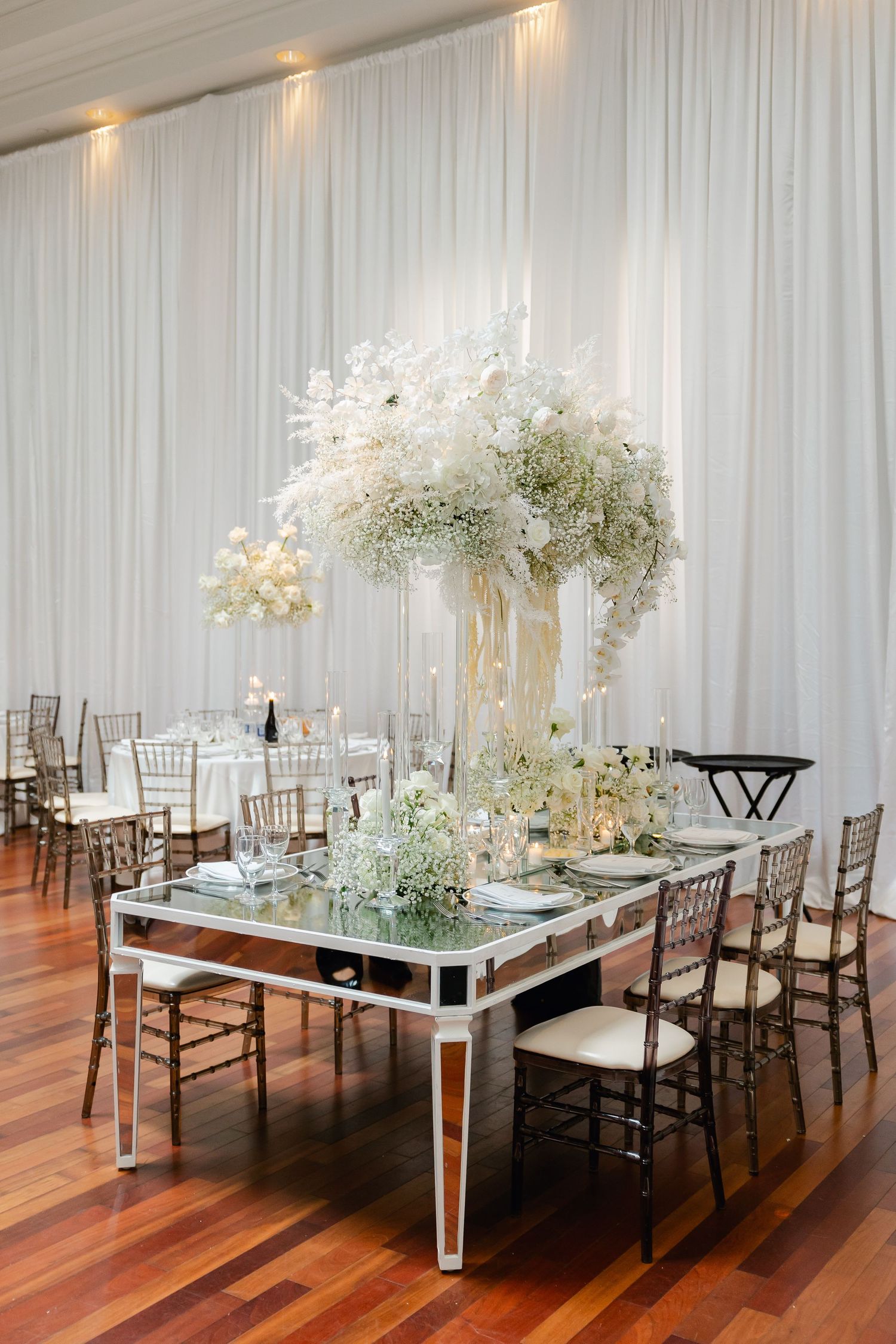 Luxurious wedding reception table with mirrored surface and tall white floral centerpiece.