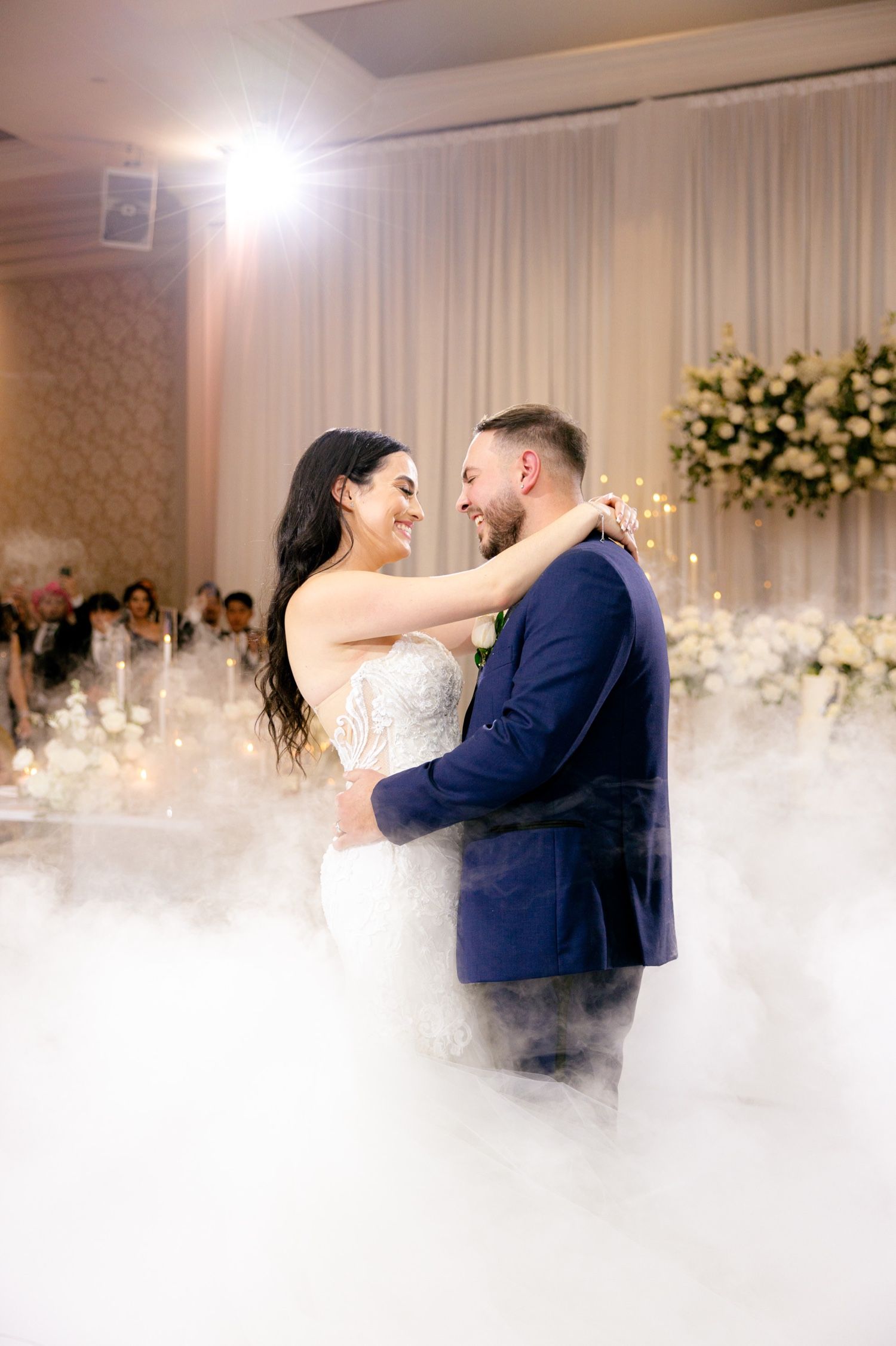 Couple sharing an intimate moment during their first dance surrounded by fog effects and floral decorations.
