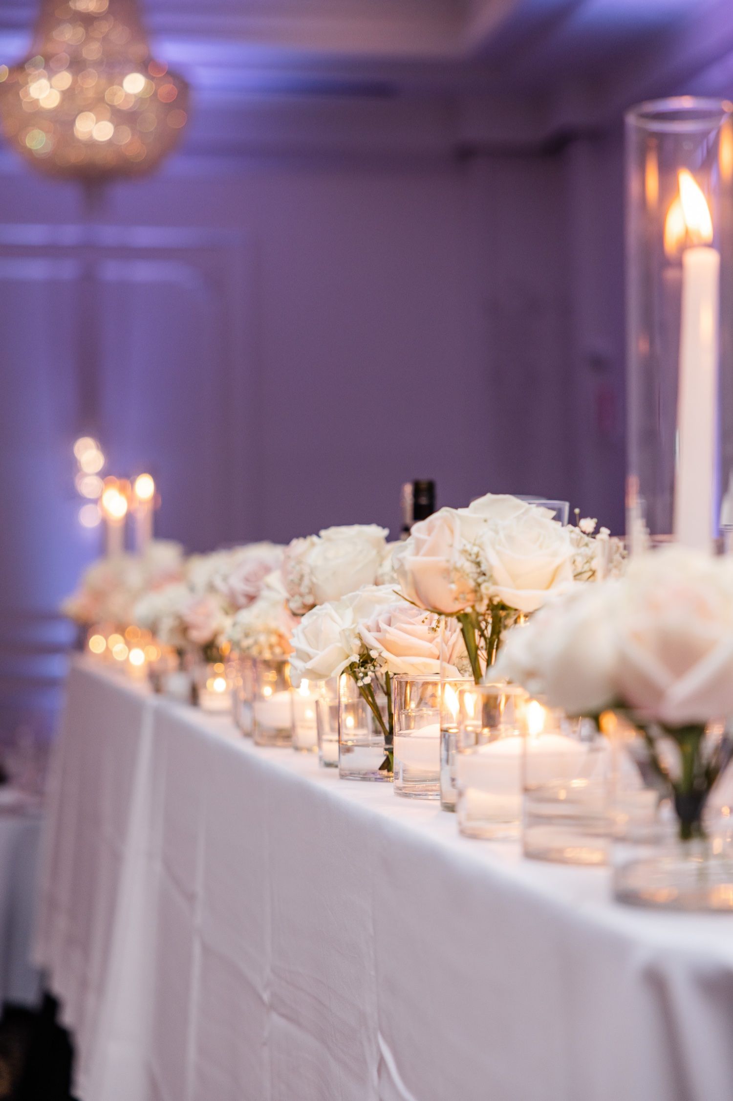 Romantic white table setting with blush roses and glowing candles for wedding reception.