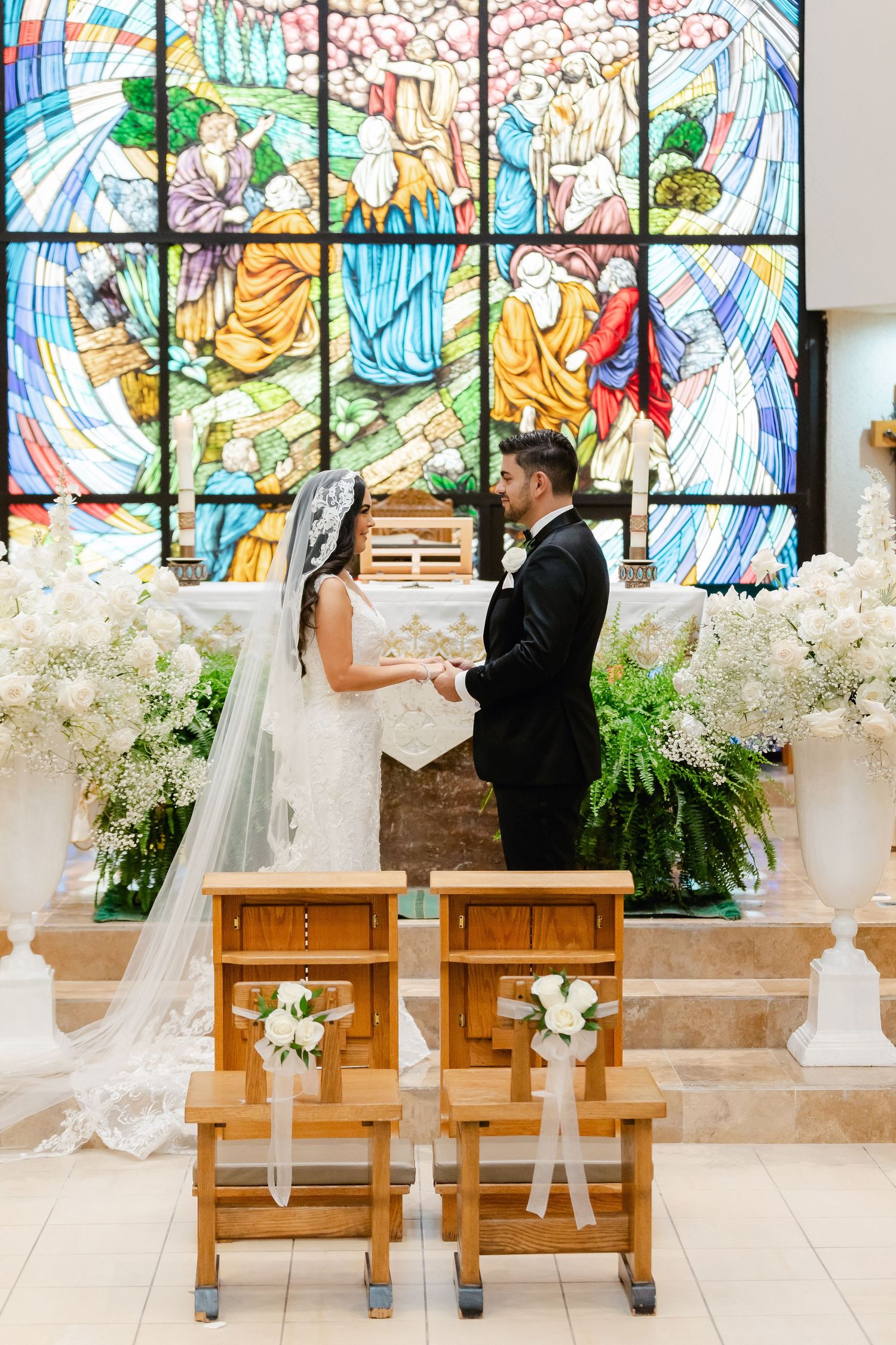Wedding ceremony with couple exchanging vows before vibrant stained glass window.