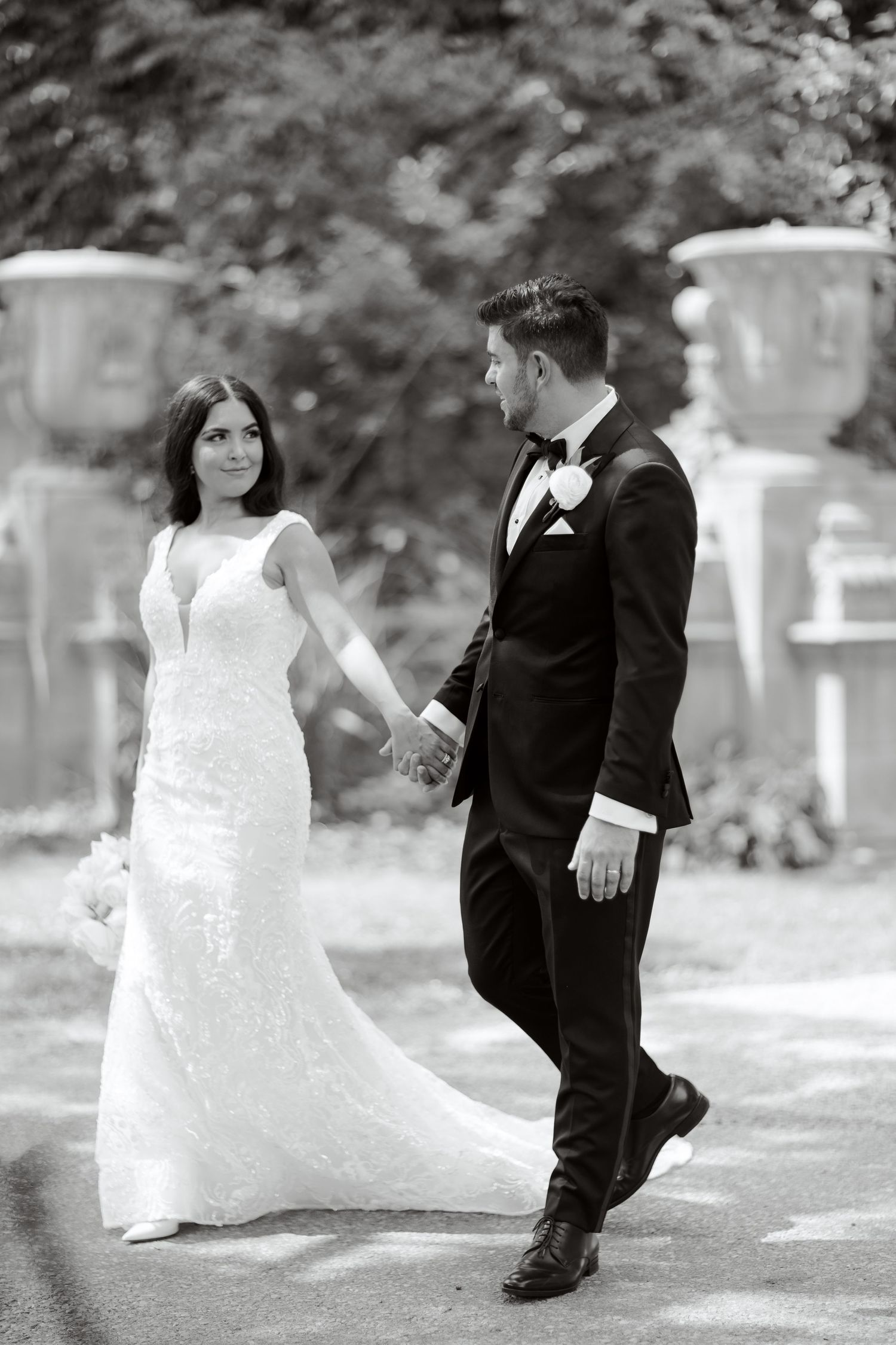 A romantic black and white wedding photo of a couple walking outdoors with decorative urns in the background.