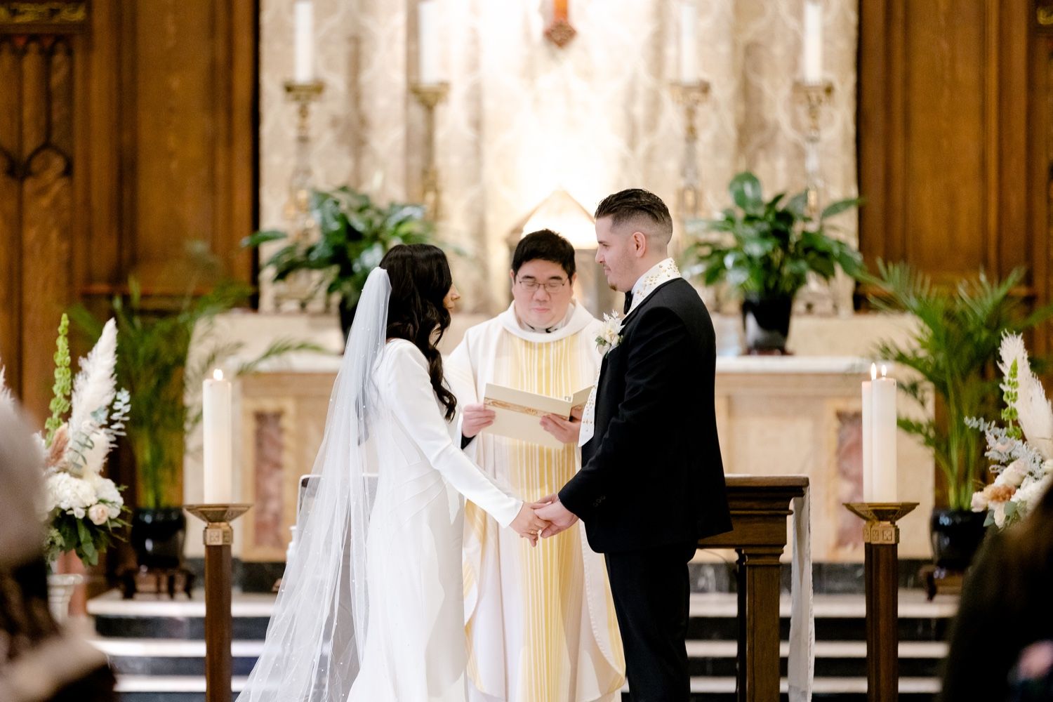 Traditional catholic wedding ceremony in ornate church with floral altar decorations.