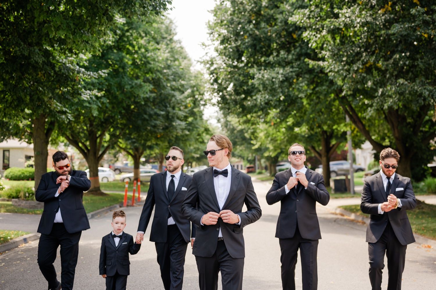 Groomsmen having fun posing while walking down a tree-lined street.