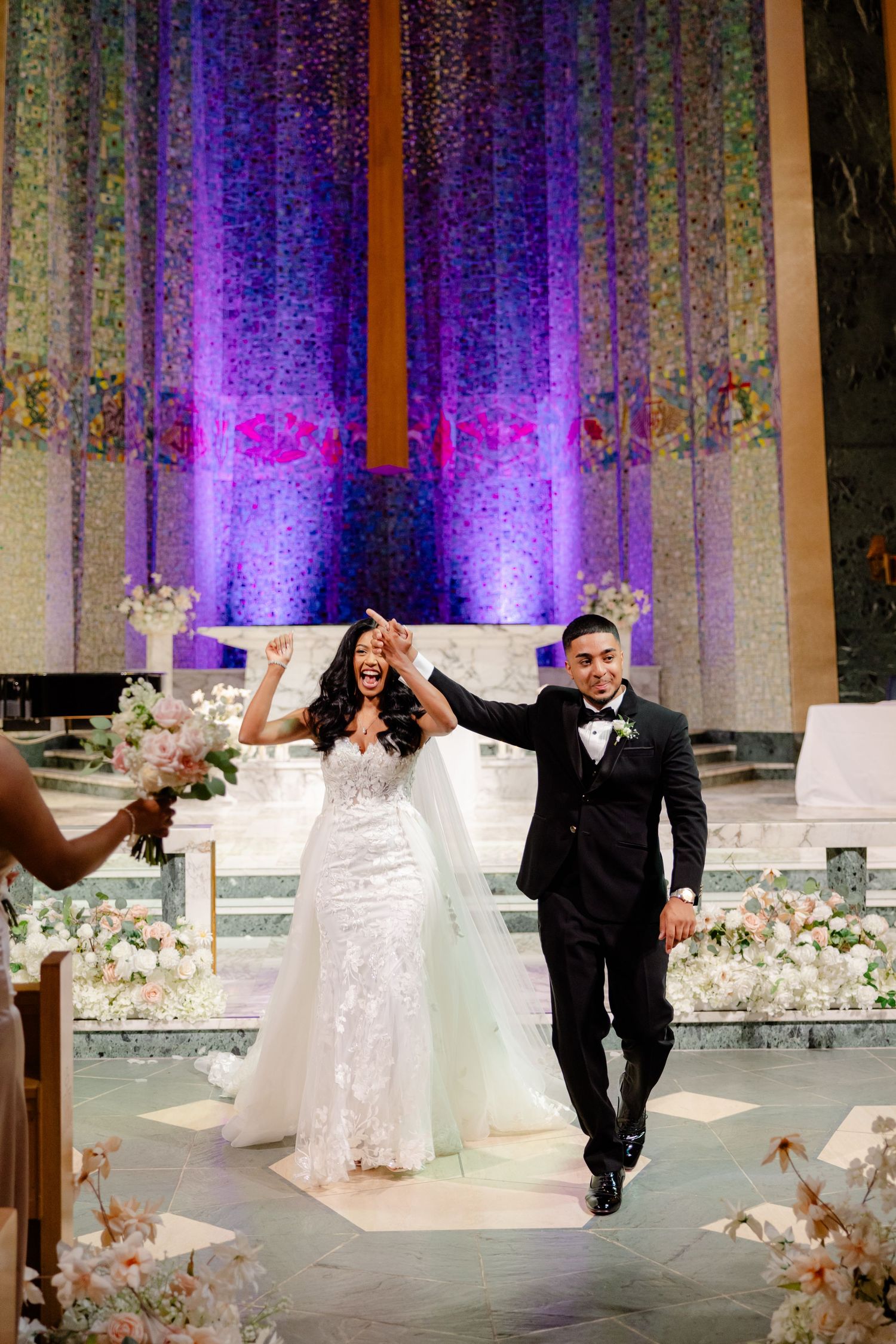 A celebratory recessional in a church with purple uplighting and floral decorations.