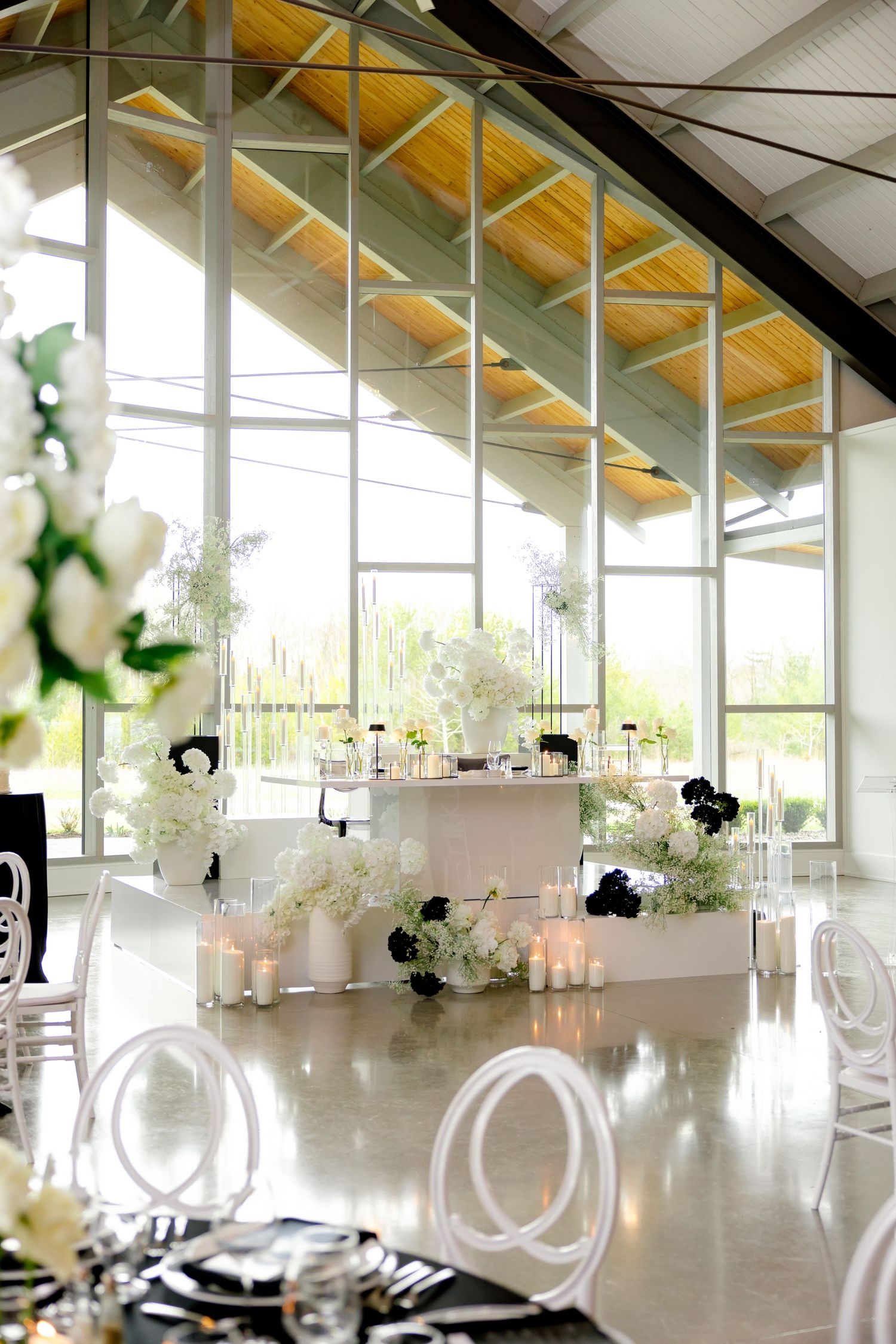 Bright wedding venue interior with vaulted ceiling, large windows, and elegant white decor.