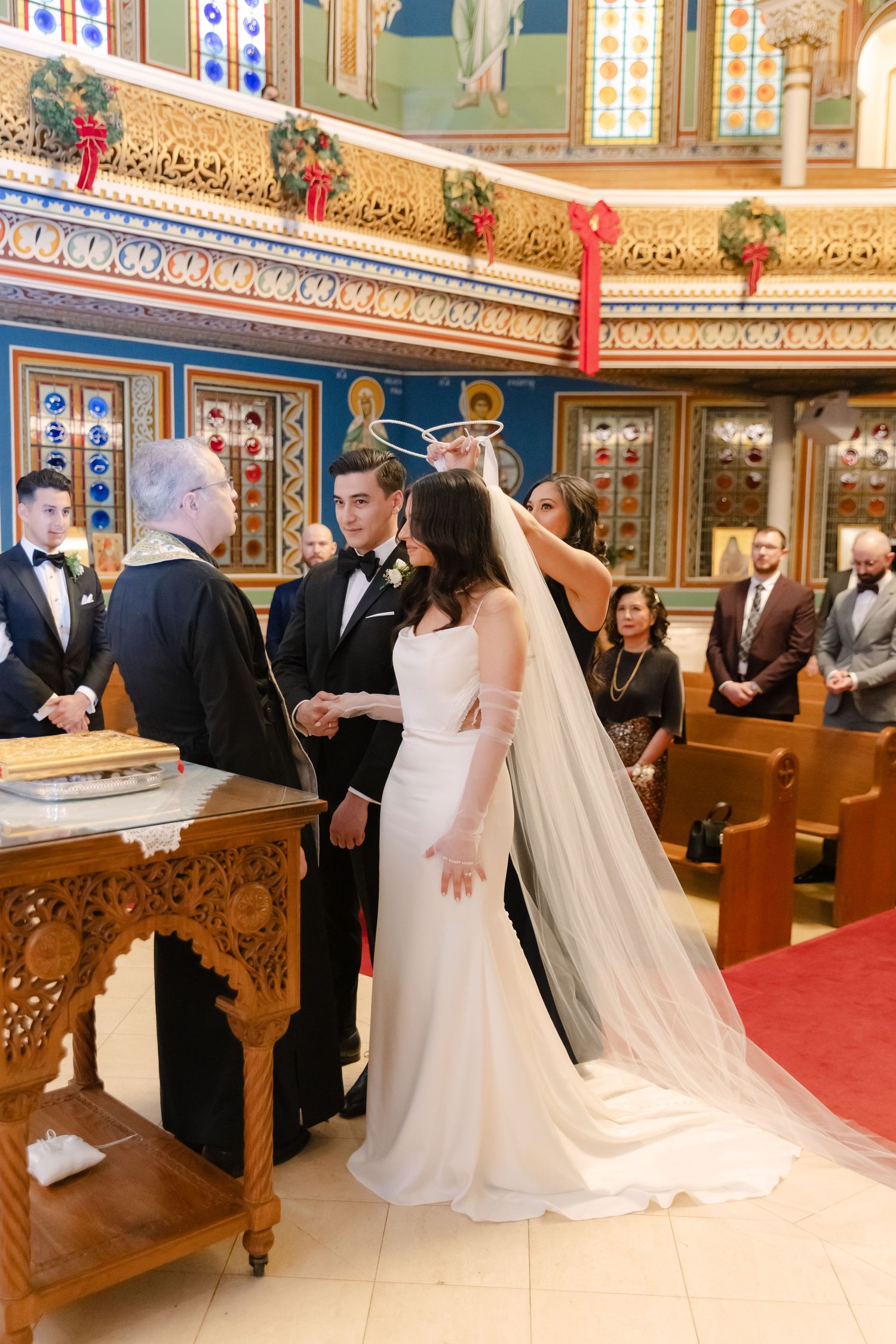 Wedding ceremony in progress at orthodox church with decorative icons and red carpet.
