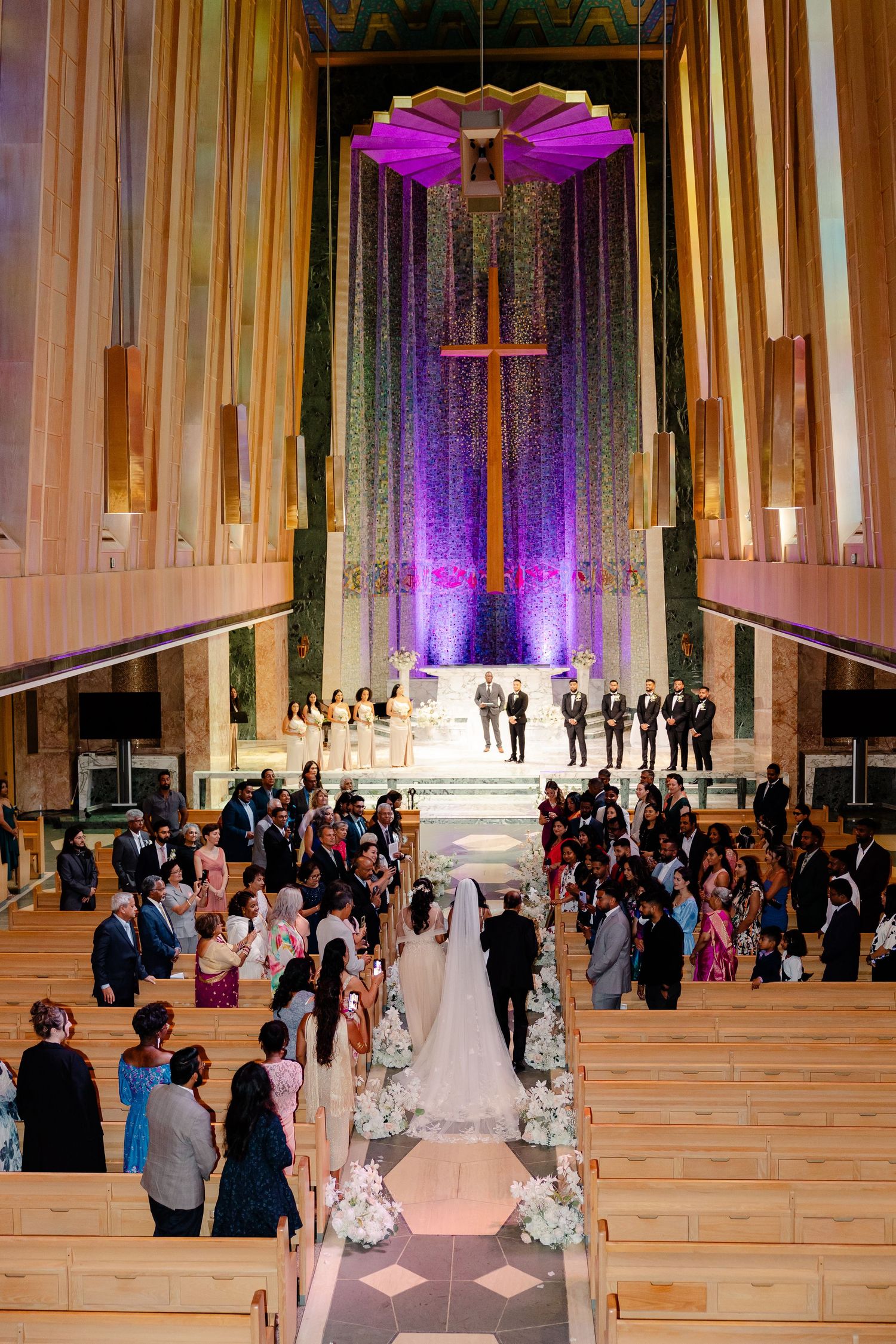 Wedding ceremony in modern church with dramatic purple lighting and high ceilings.