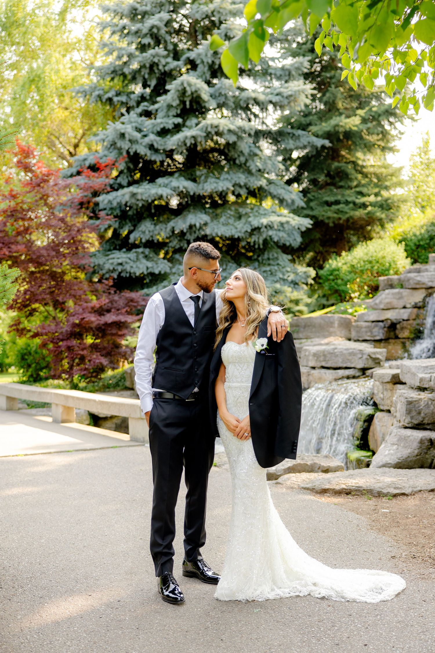 Relaxed wedding photo with couple sharing tender moment by garden waterfall.