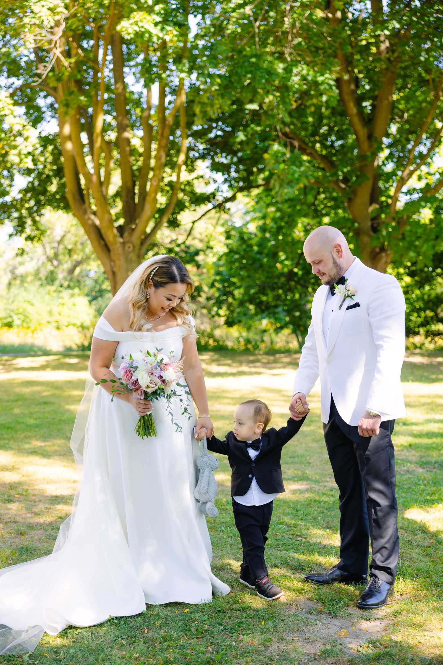 Candid wedding moment on sunny day with couple and playful toddler on lawn.